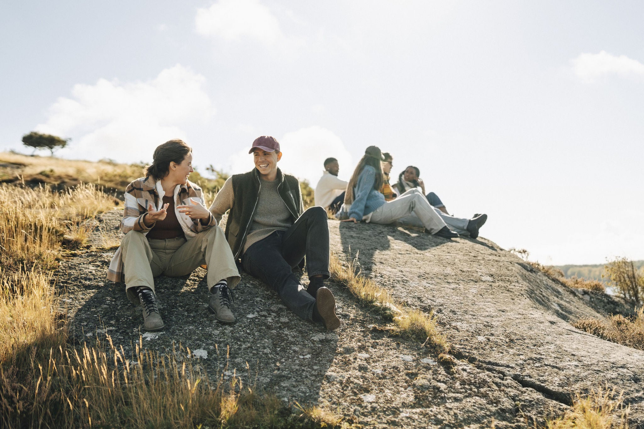 Happy young man talking with female friend while sitting on hill at sunny day
