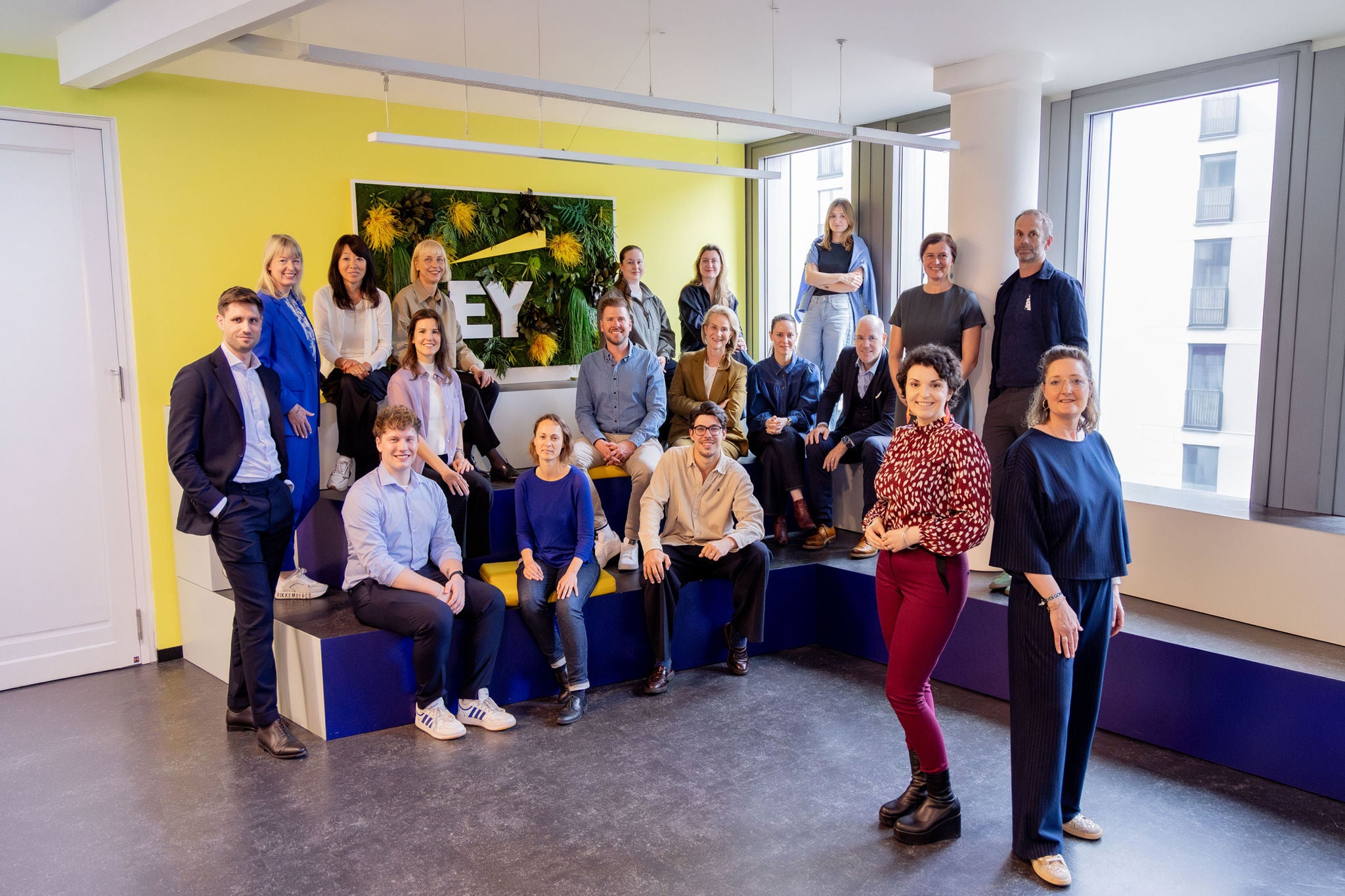 Gruppenaufnahme eines Teams in einem modernen Büro mit EY-Branding und Pflanzenwand.