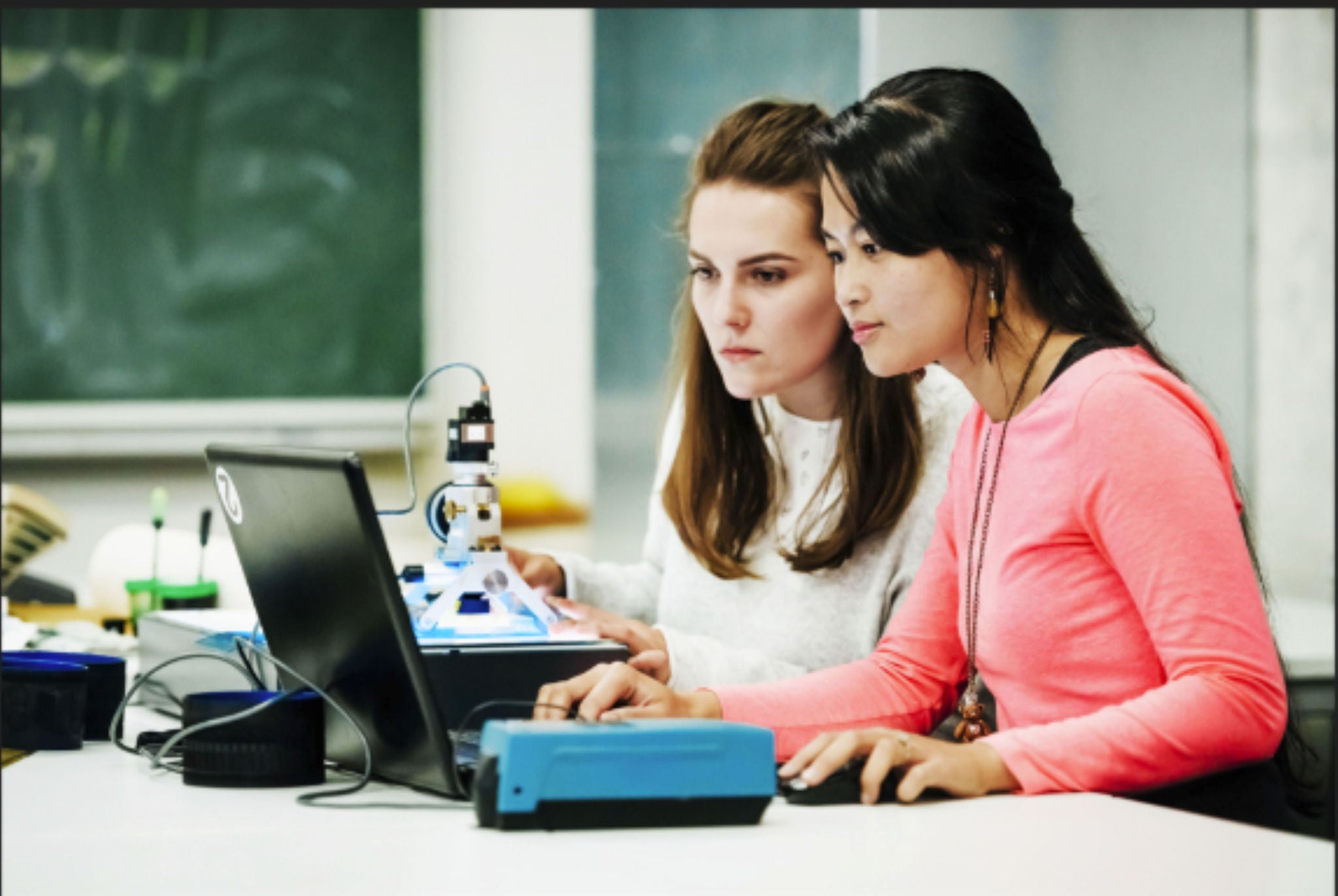 Two people working together at a desk with laptops and lab equipment