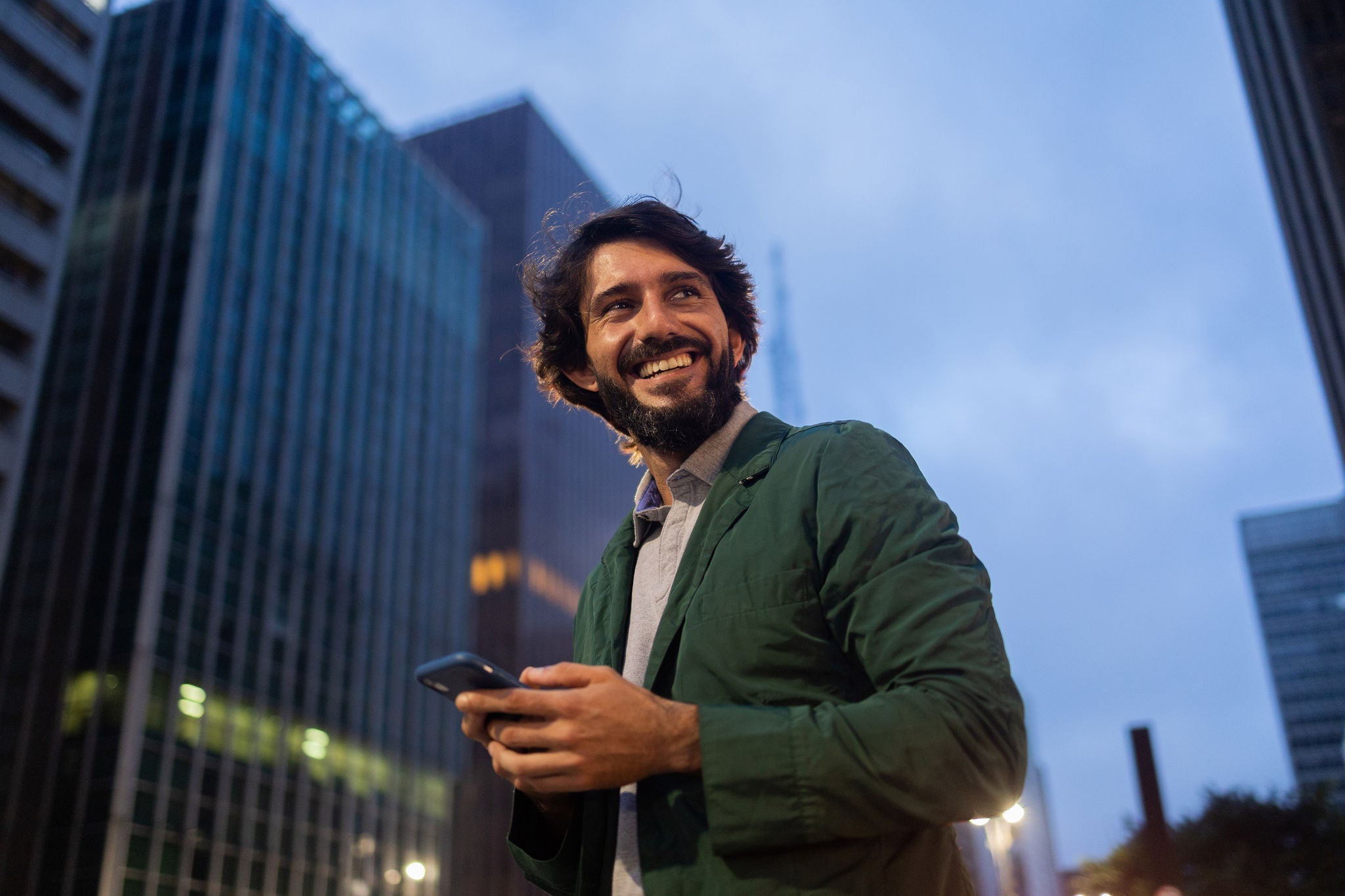 Jonge man gebruikt een smartphone terwijl die in een stadsstraat staat met hoge gebouwen
