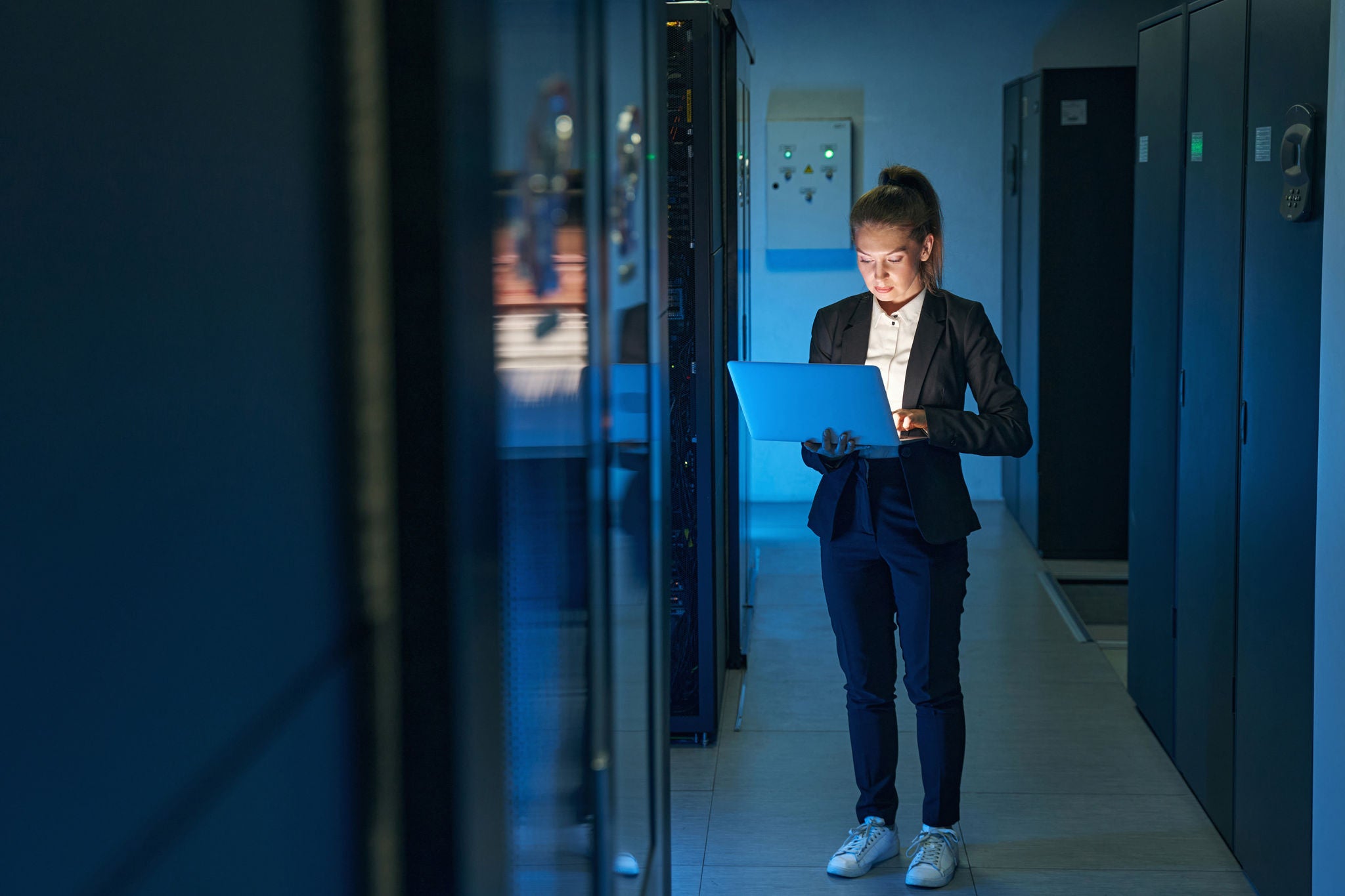 Female technician walking through a data center while checking a laptop