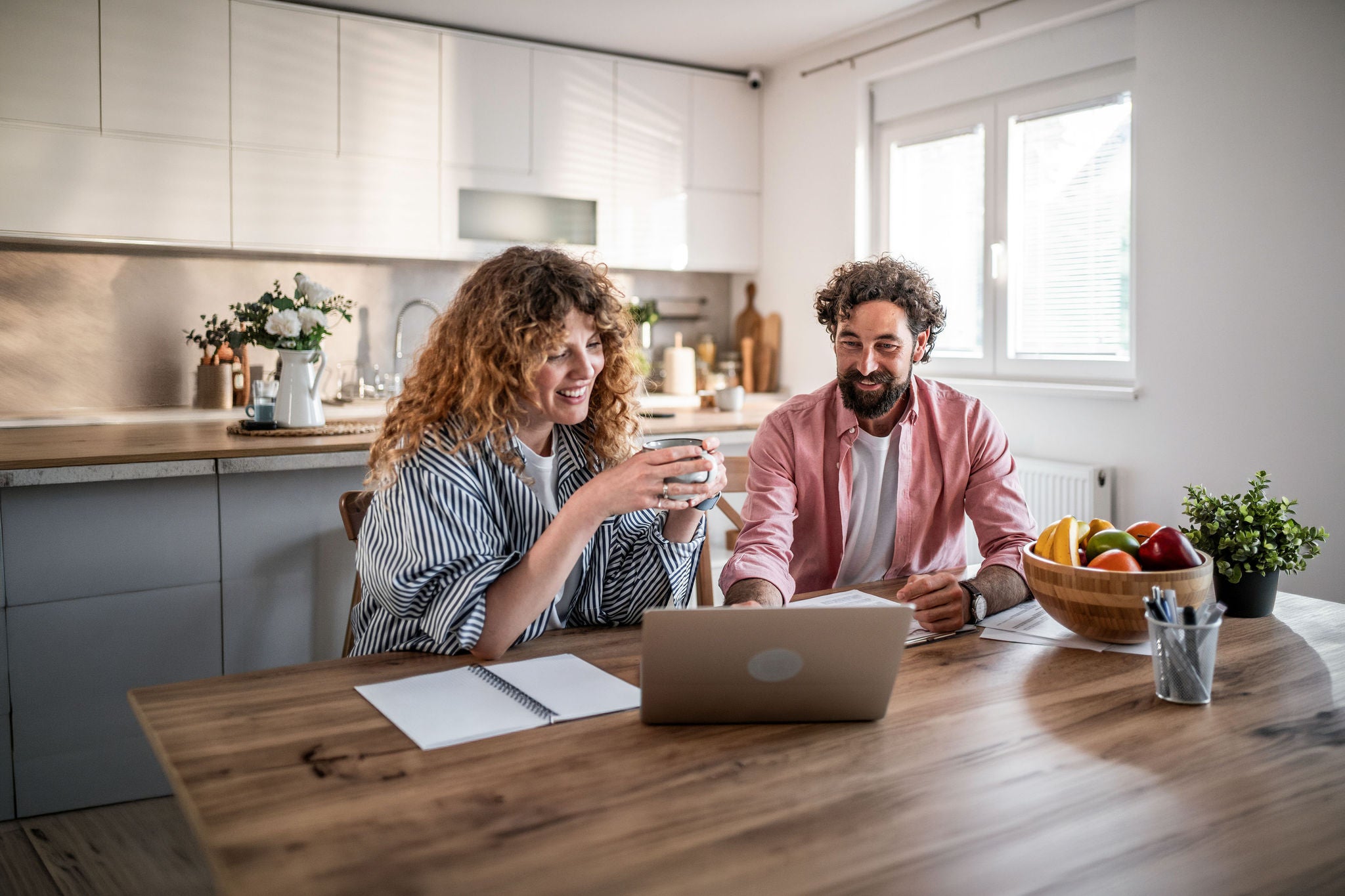 Smiling young couple at kitchen table using laptop and plan finances together.