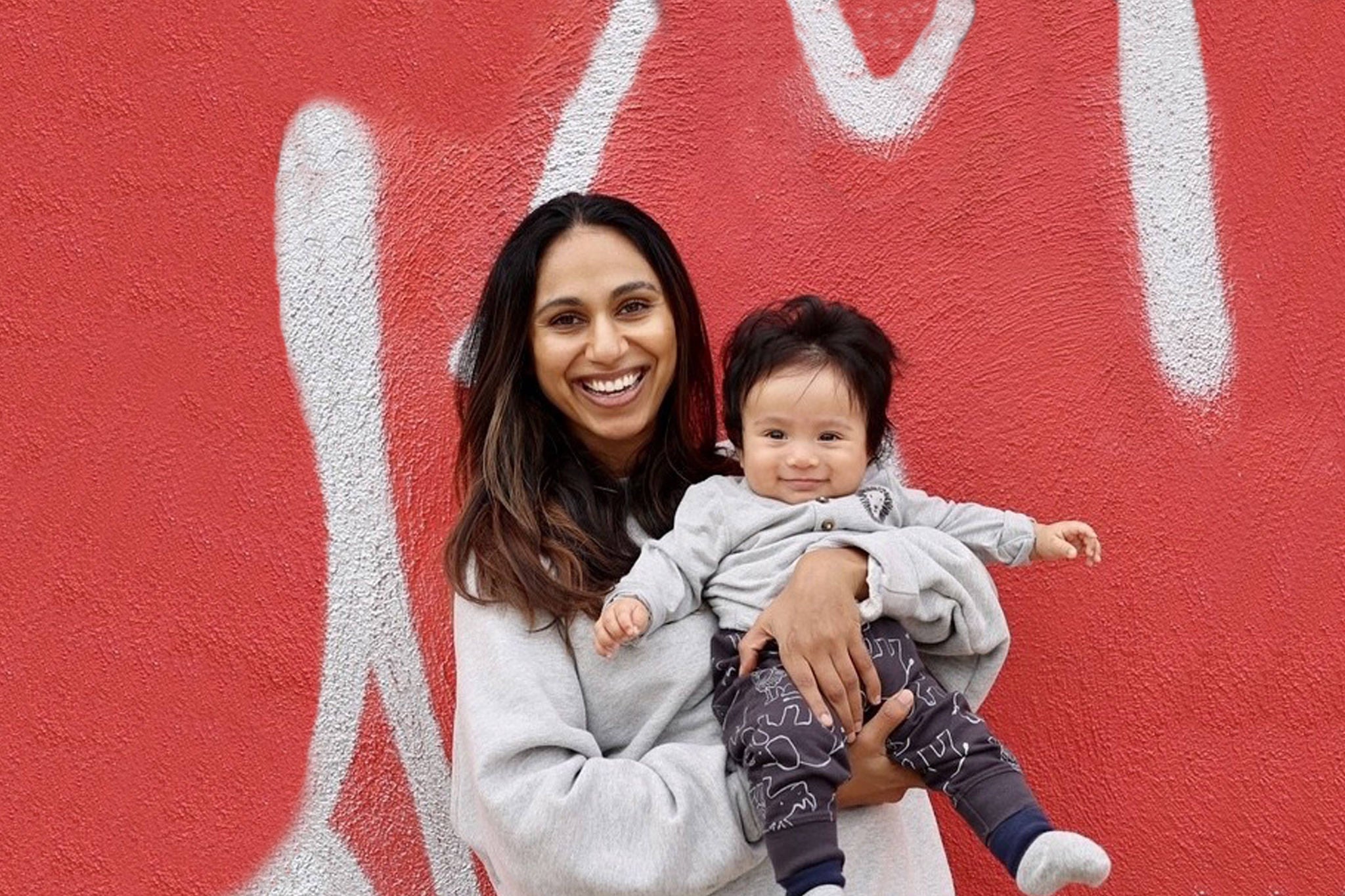 Sonia Parikh holding a child in front of a wall with graffiti 