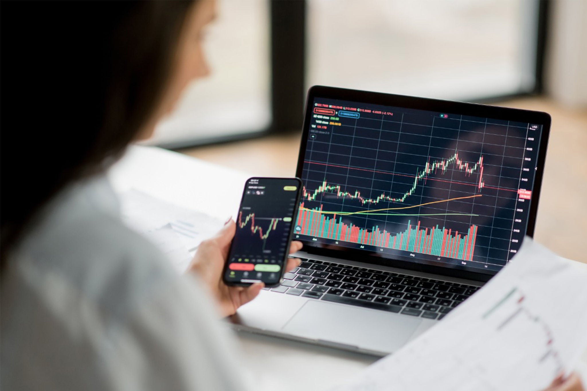 mujer viendo laptop y balores de acciones
