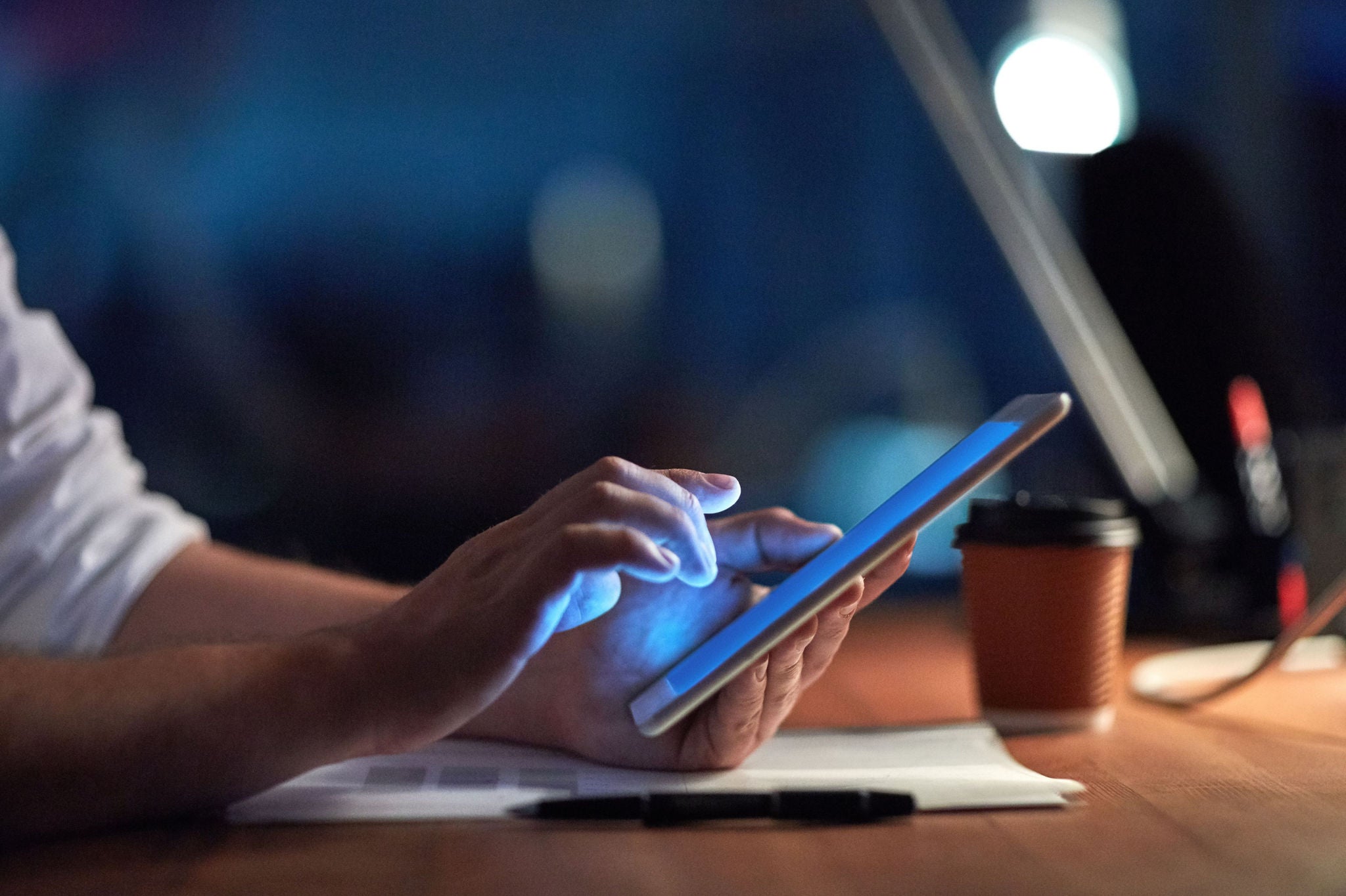 Main utilisant une tablette sur un bureau près d’un café