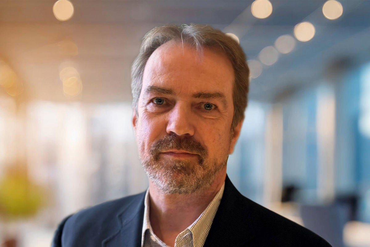 Eine Person in Businesskleidung steht vor einem hellen Bürohintergrund mit dekorativen Lichtpunkten.