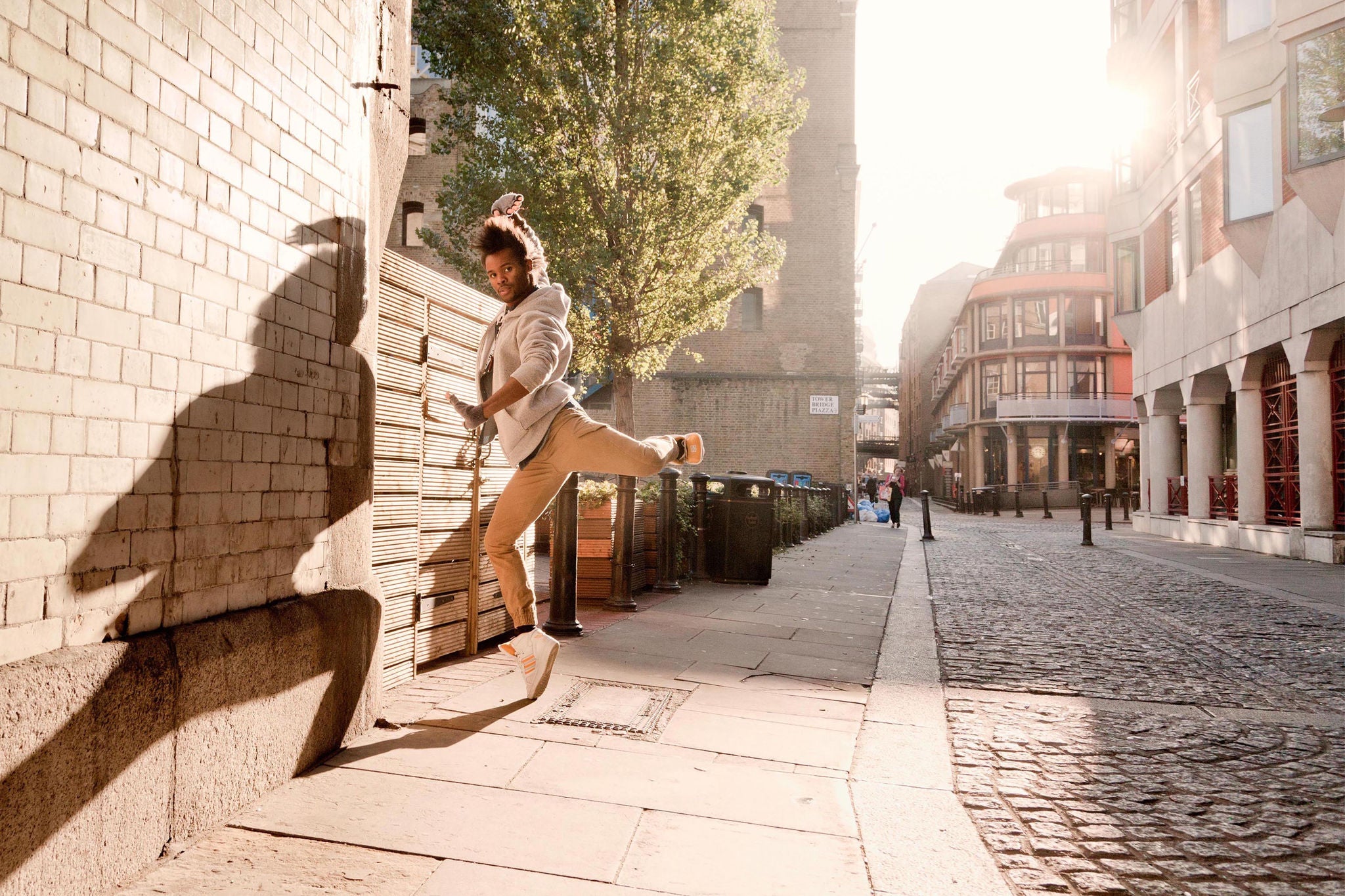 Young man at morning light shines on street dancer creating striking shadow on wall.