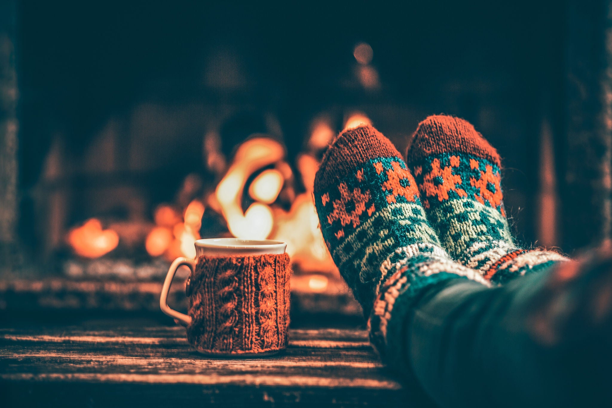 Warm patterned socks and a hot drink beside a fireplace