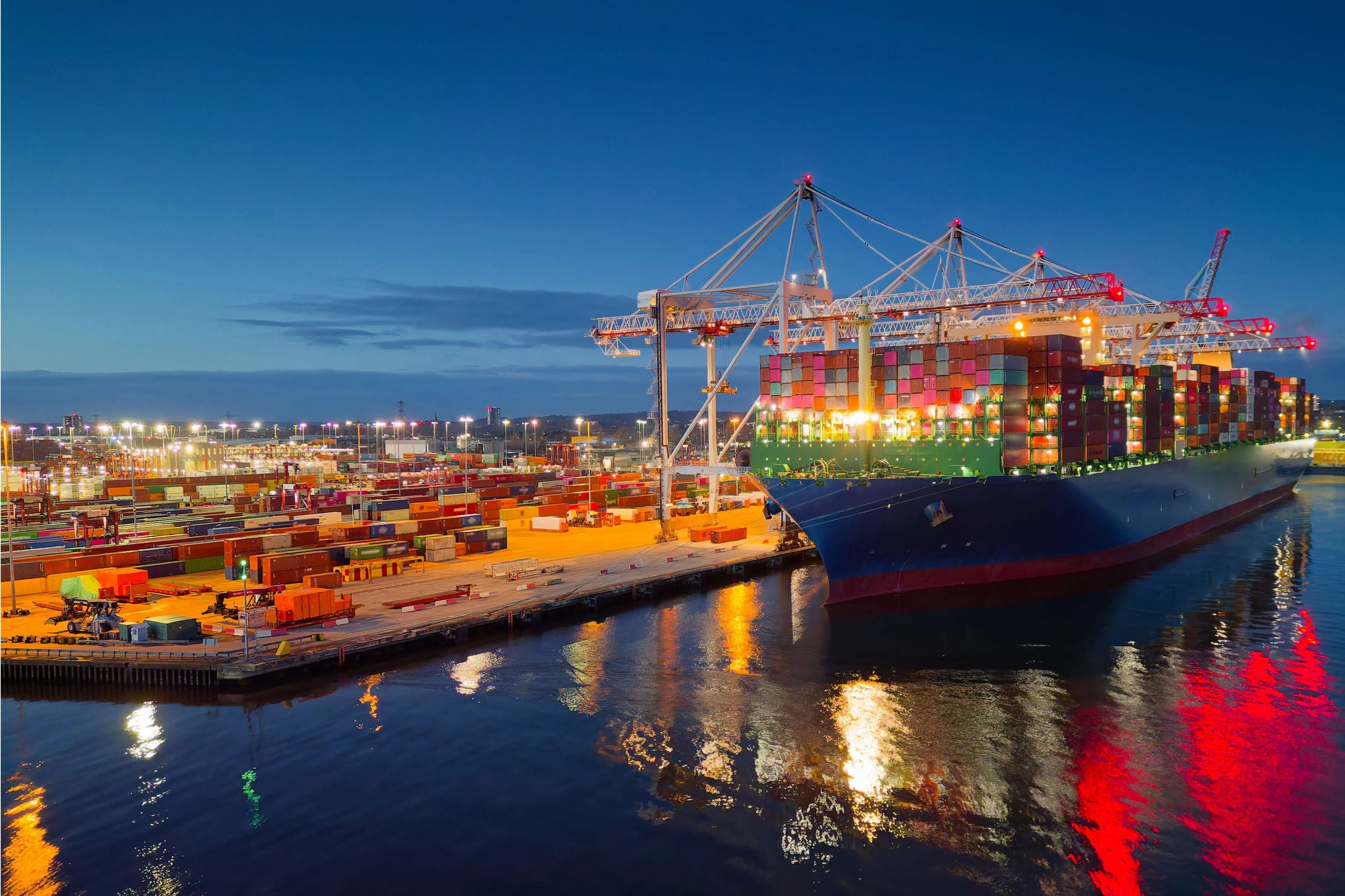Illuminated Southampton UK container terminal with large container ship at dusk