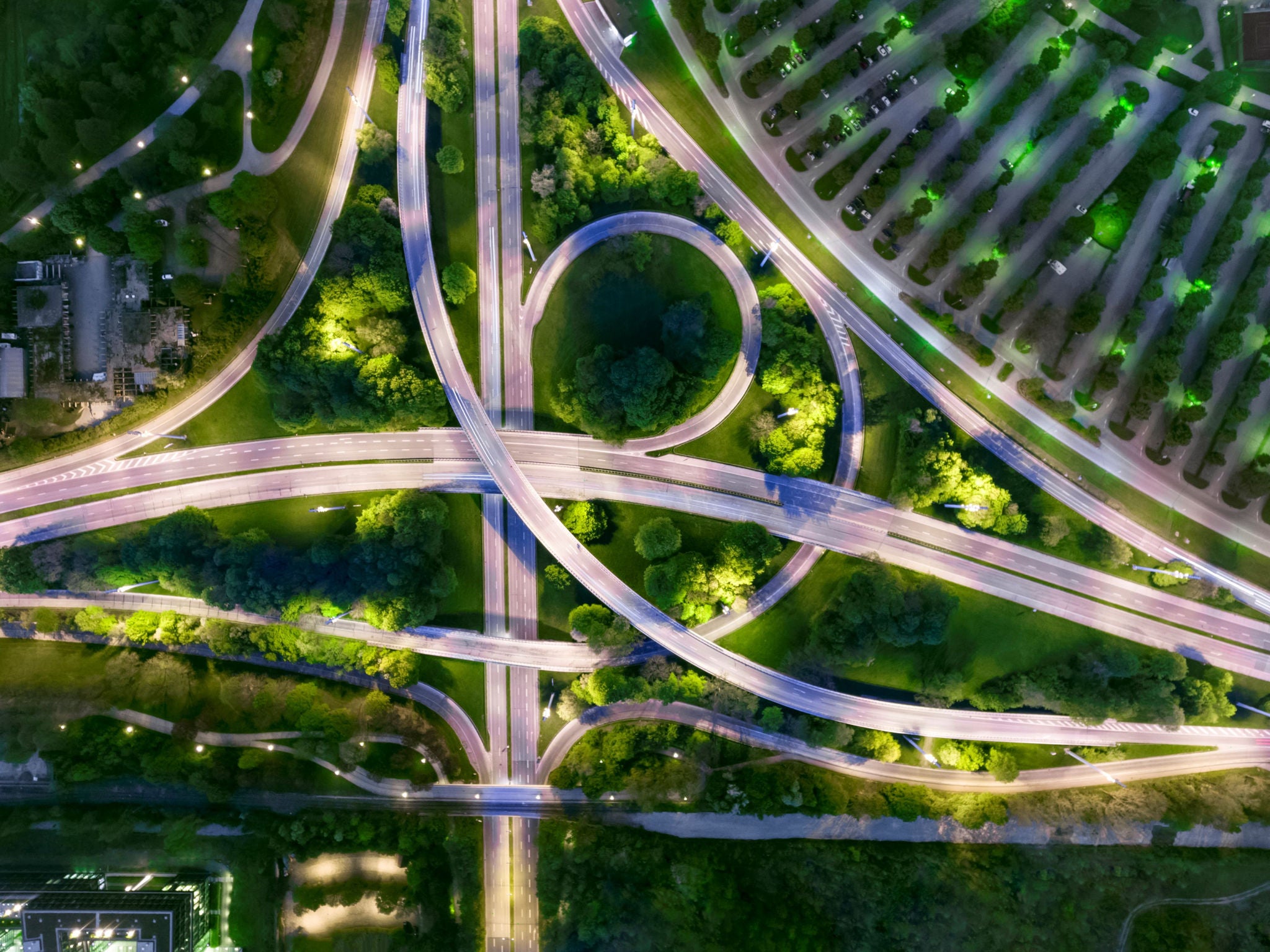 Látványos éjszakai légifelvétel egy többszintű autópálya‑csomópontról, amelyet gazdag zöldterület vesz körül.