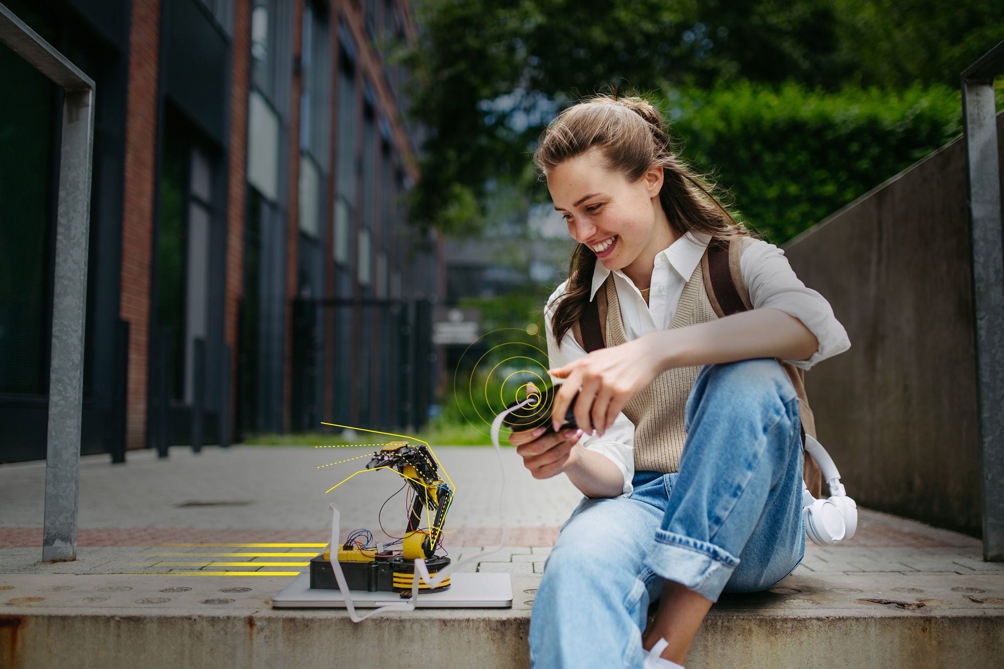 student on campus using a handheld controller to operate a small robotic arm outdoors