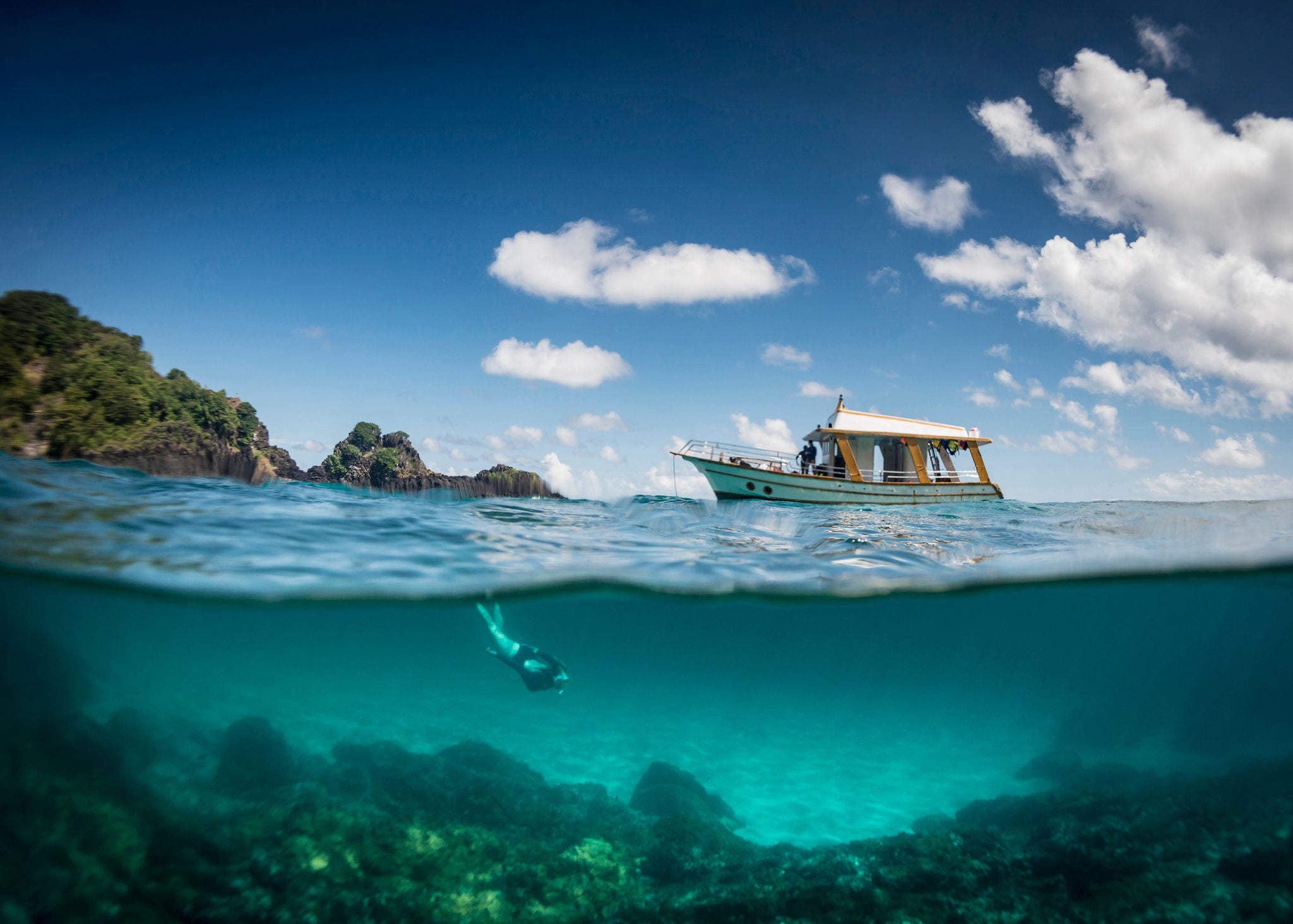View of a tour boat and a woman free diving at 'Sancho' beach in the archipelago of Fernando de Noronha - Brazil