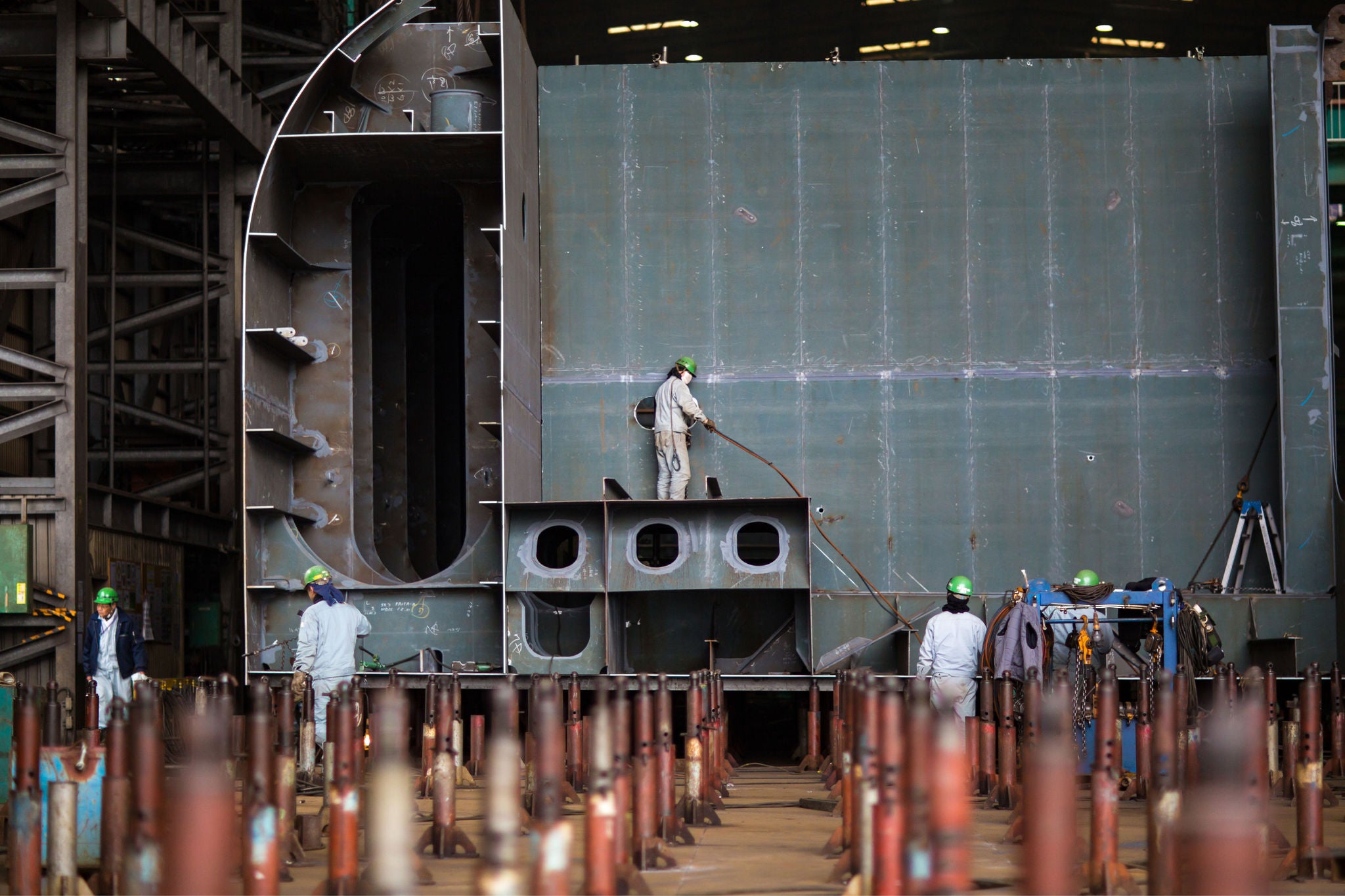 Workers assembling a large steel structure in a shipyard