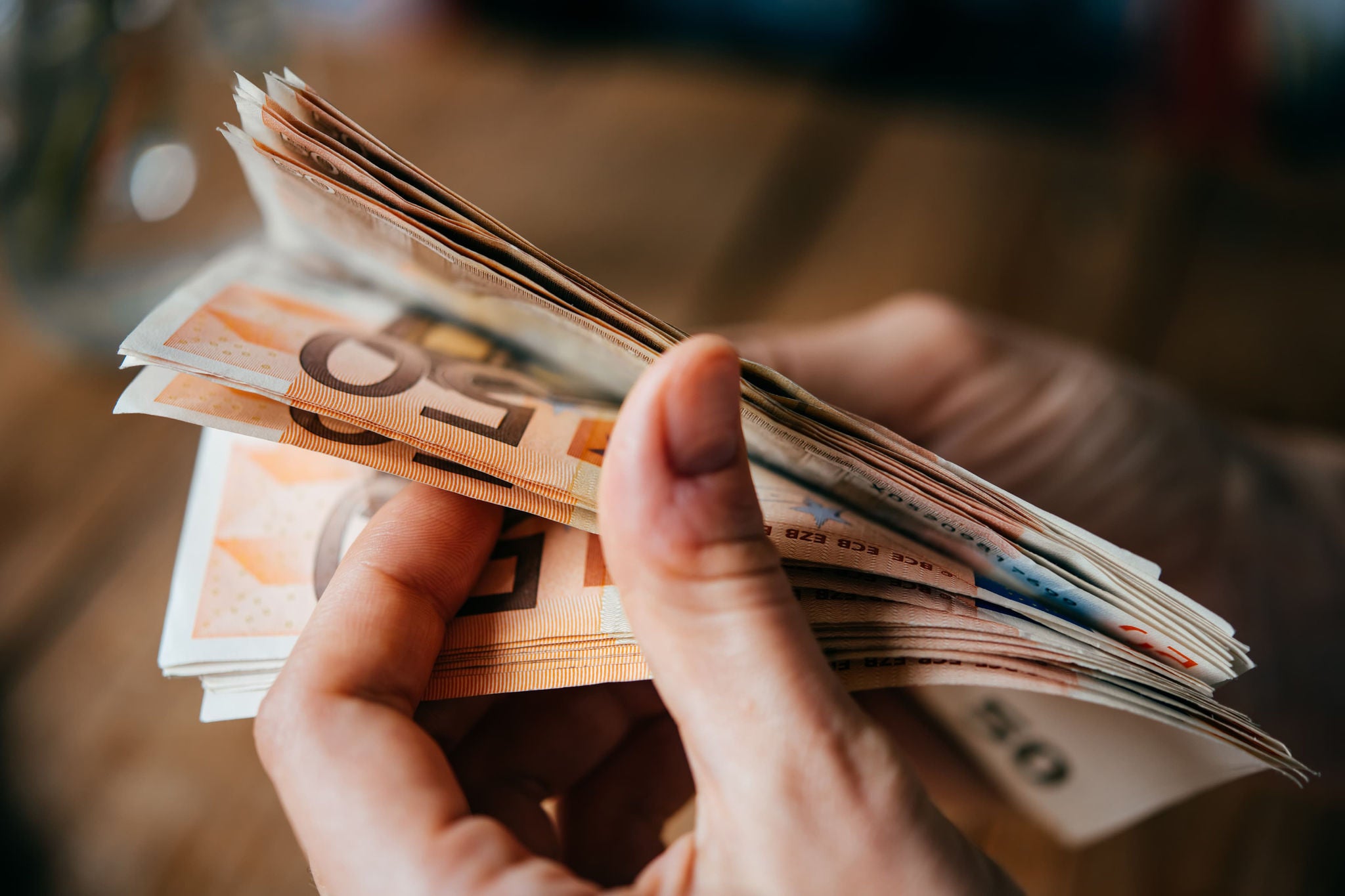 Hände zählen Euro-Banknoten in einer Nahaufnahme mit unscharfem Hintergrund.