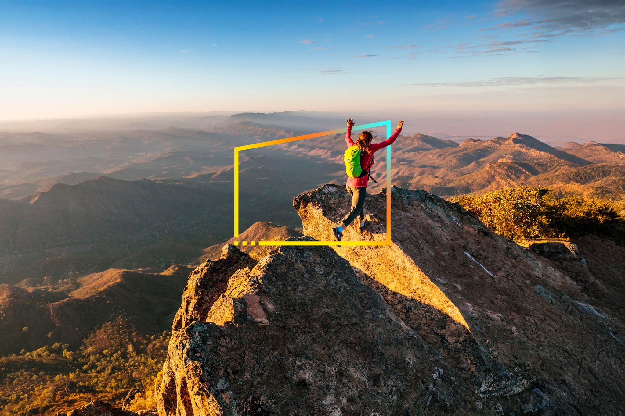 A woman leaps across a gap in the rocky ridge on top of St Mary Peak at sunrise, the highest point in the Flinders Ranges National Park, South Australia