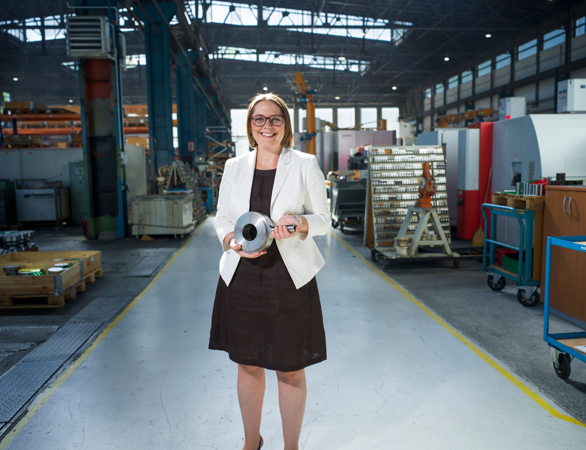Unternehmerin steht in der Produktionshalle mit Gerät in der Hand