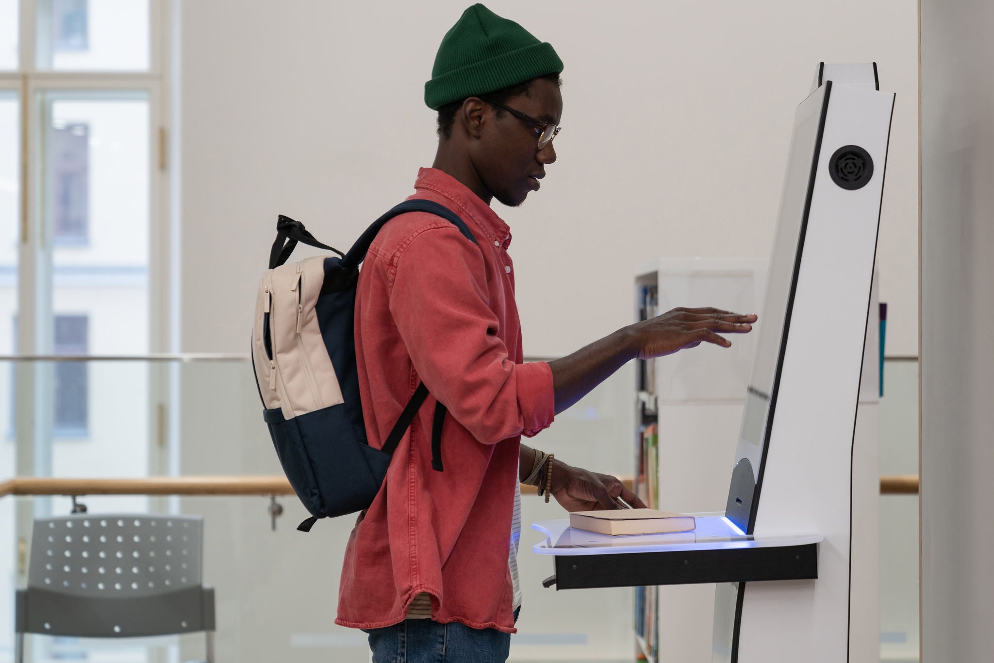 Student met rugzak gebruikt een zelfbedieningsterminal in de bibliotheek
