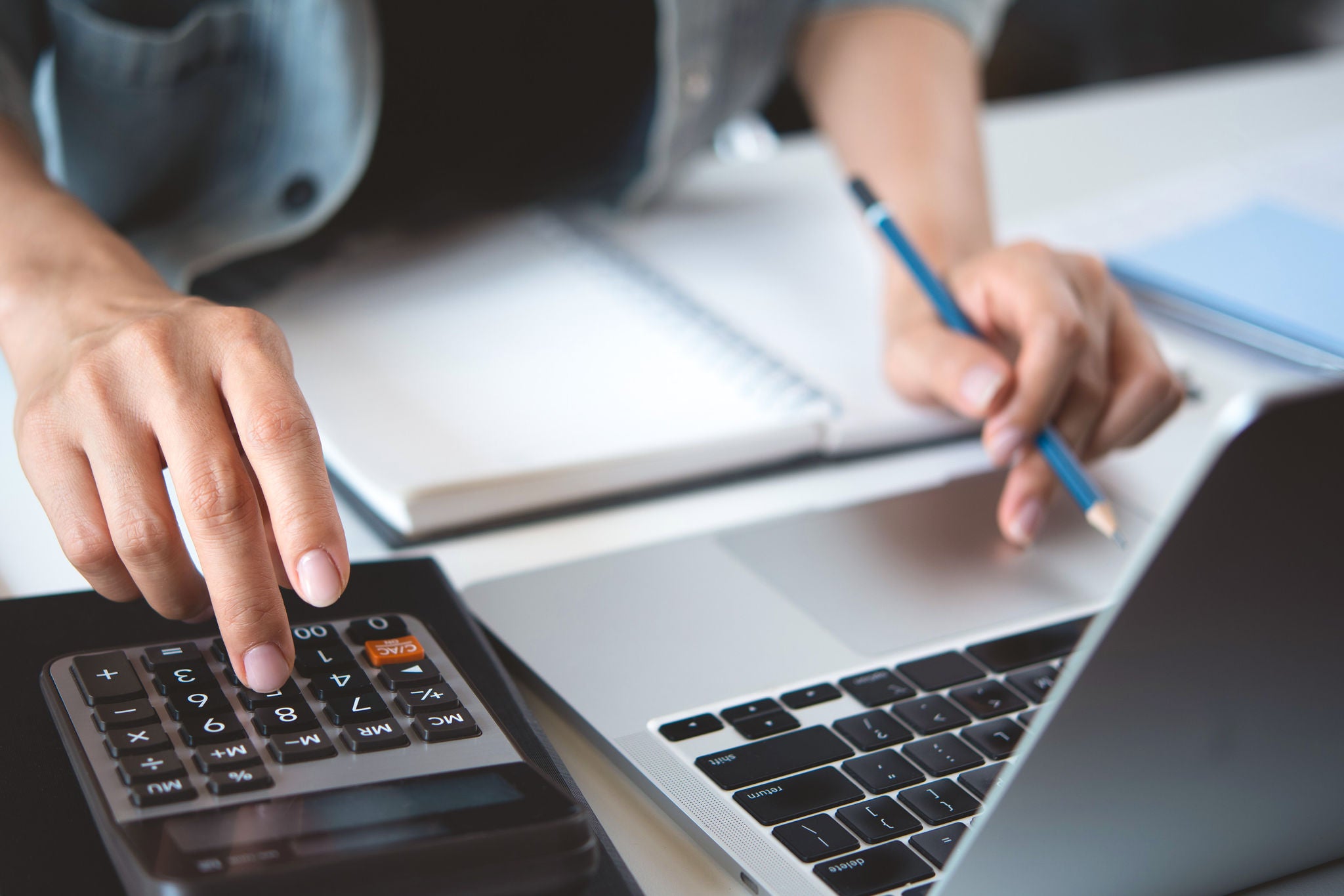 Person sitzt vor einem Laptop und rechnet nebenbei etwas am Taschenrechner aus