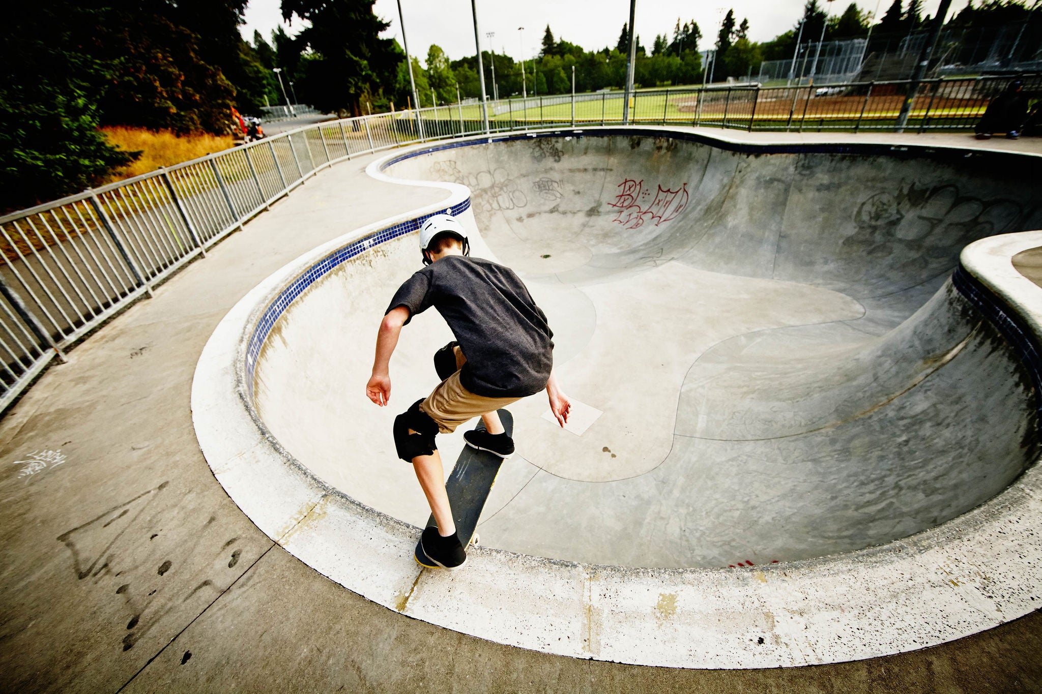 Young male skateboarder dropping into bowl of neighborhood skate park