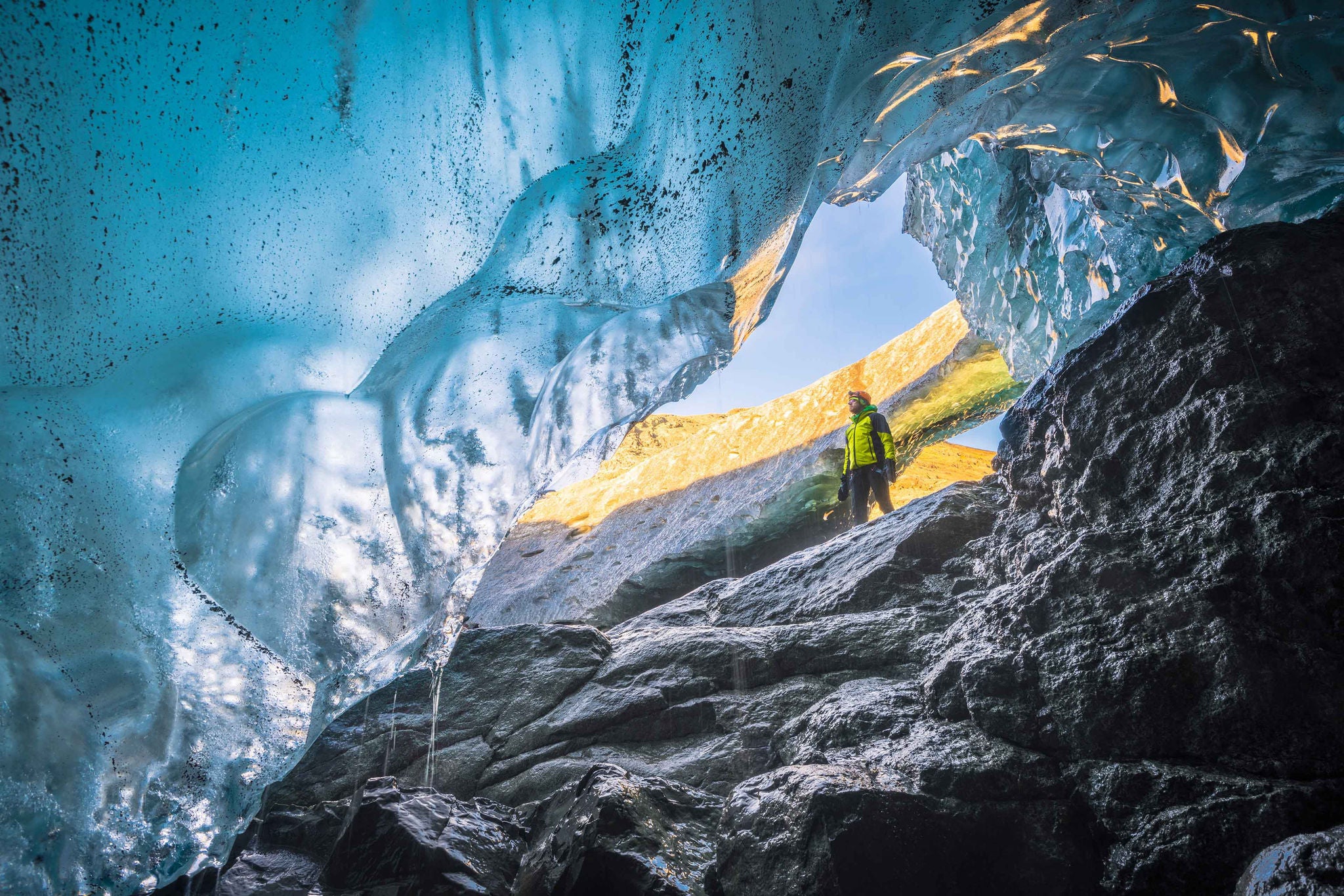 Man standing at the entrance of a crystal ice cave in Vatnajokull glacier.