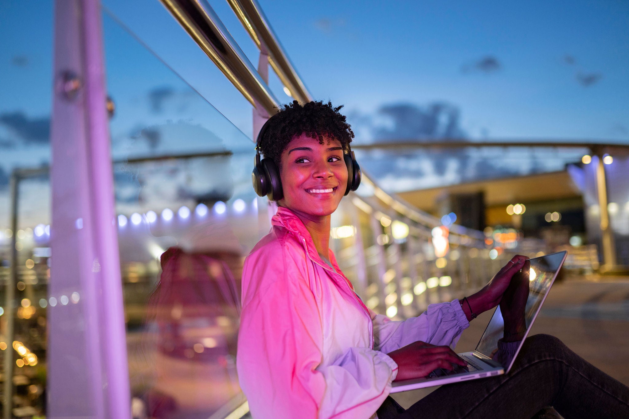 woman-with-laptop-looking-away-while-listening-music-on-headphones