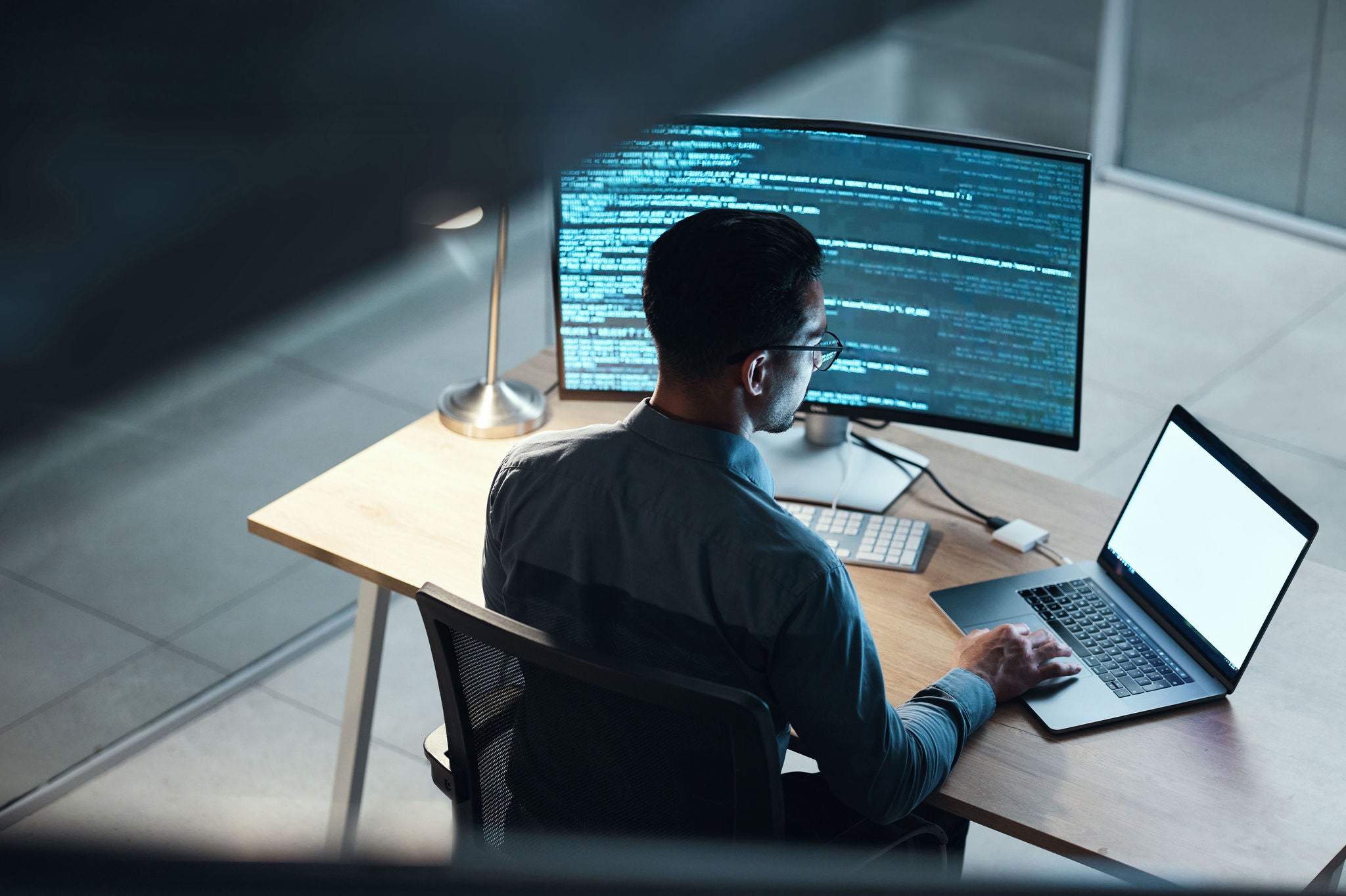 Person arbeitet an Schreibtisch mit großem Monitor und Laptop in moderner gut organisierter Umgebung