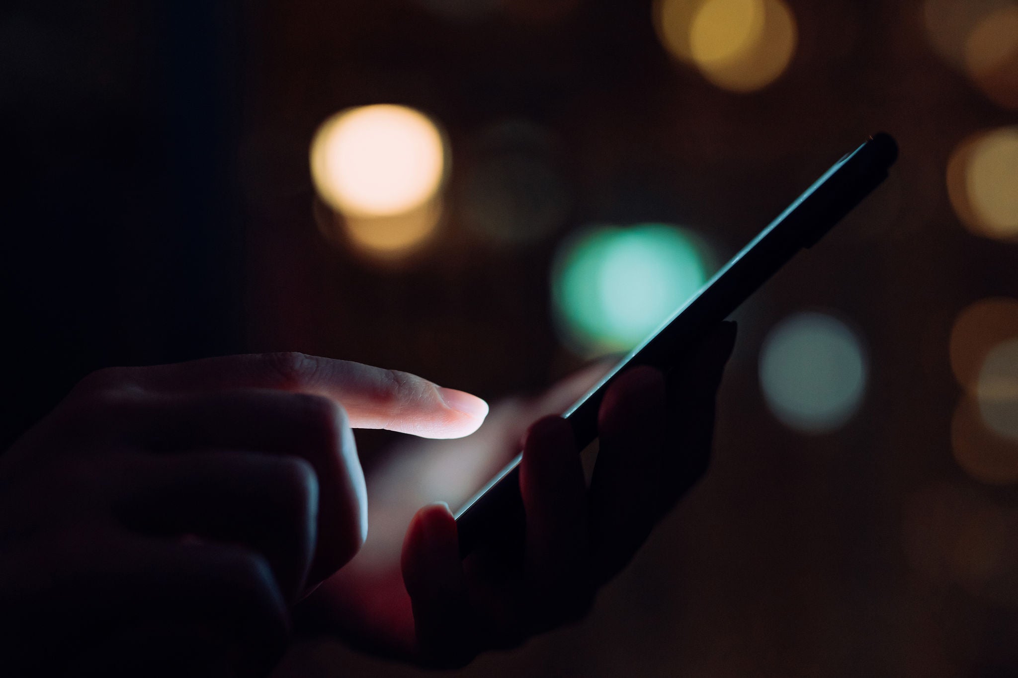 Close up of woman's hand using smartphone in the dark, against illuminated city light