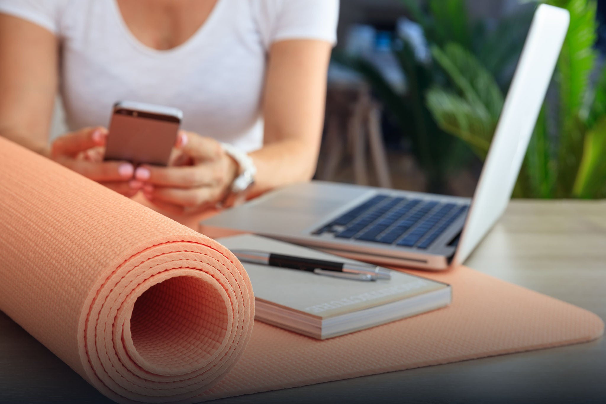 A smiling young woman with headphones and folders, standing outdoors on a college campus.