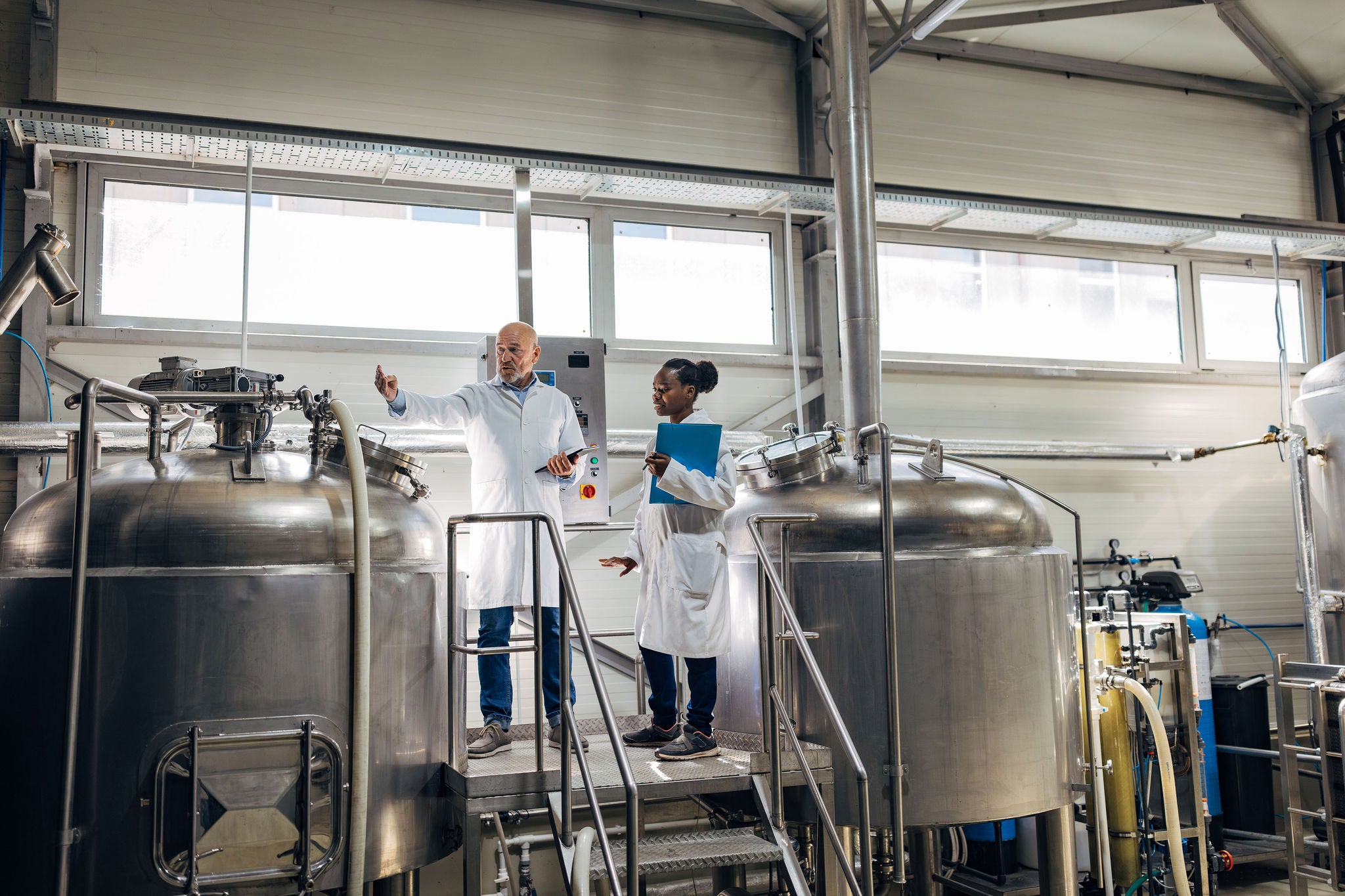 A senior brewery technologist explains to a younger female colleague how the beer filtering and brewing machine works