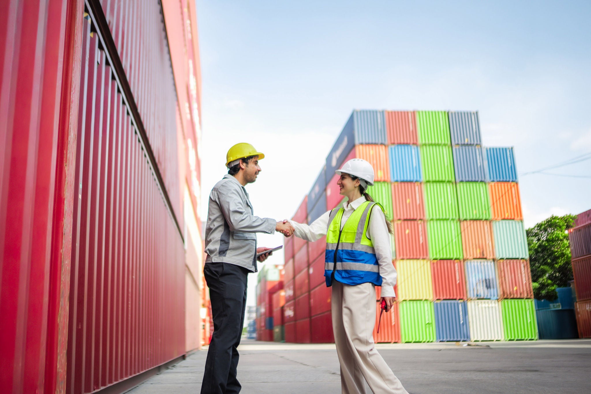 Two logistics workers shake hands beside shipping containers after inspection, showing supply chain trust ops