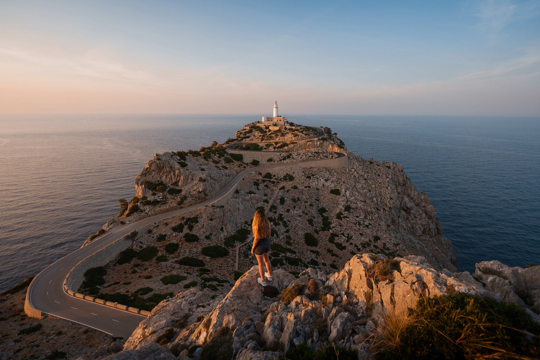 Young woman standing on a cliff looking at cabo formentor lighthouse