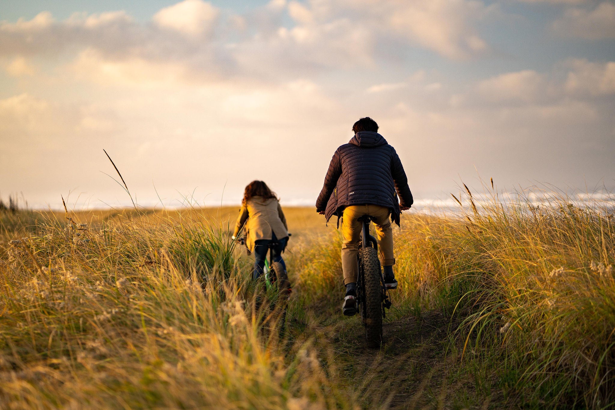 couple ride bicycles through grassy headlands above the ocean