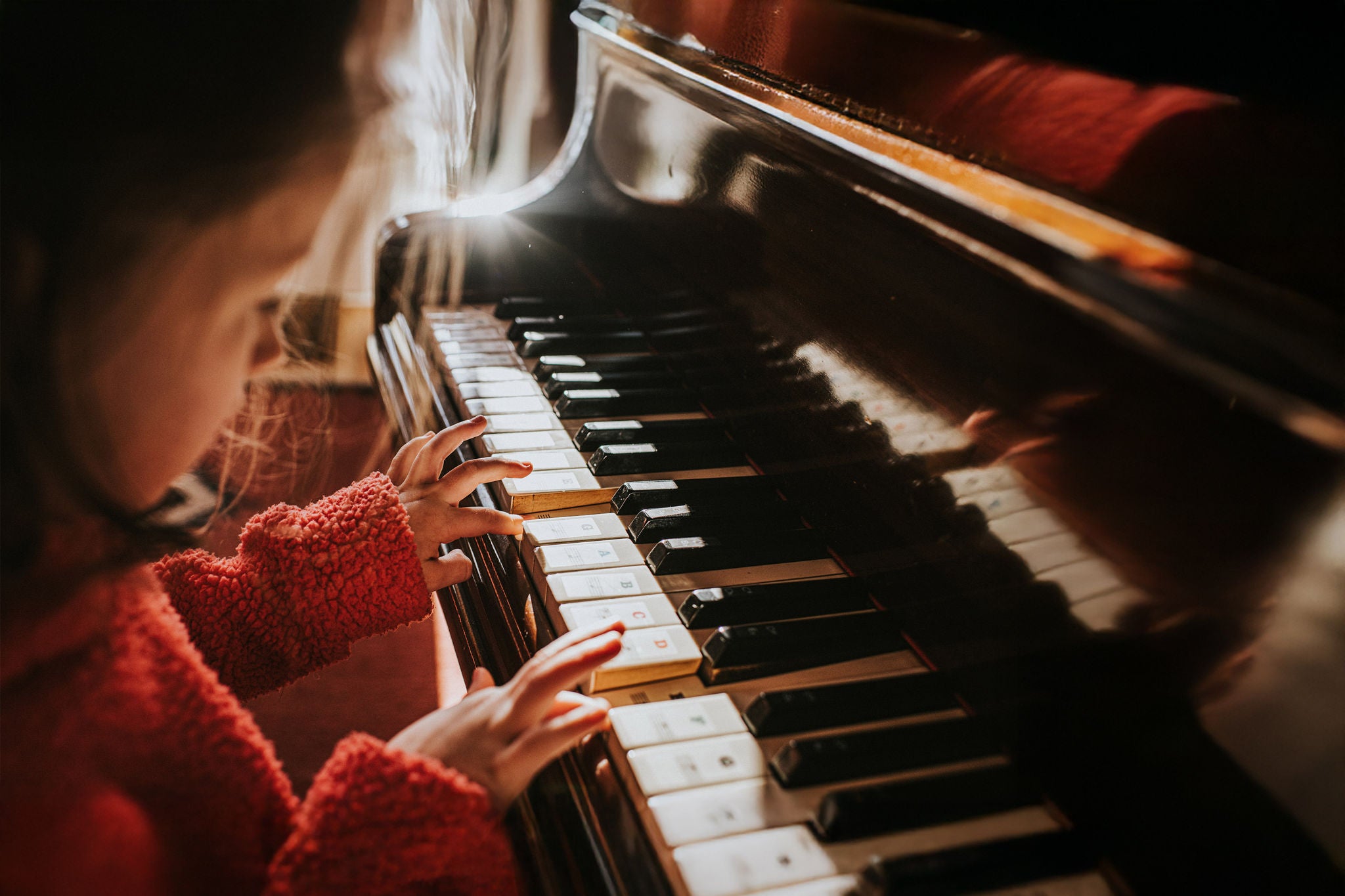 Cute little pre-school age girl playing a wooden baby grand piano in a sunny domestic environment. Top down image focusing on her little hands on the piano keys. Space for copy.