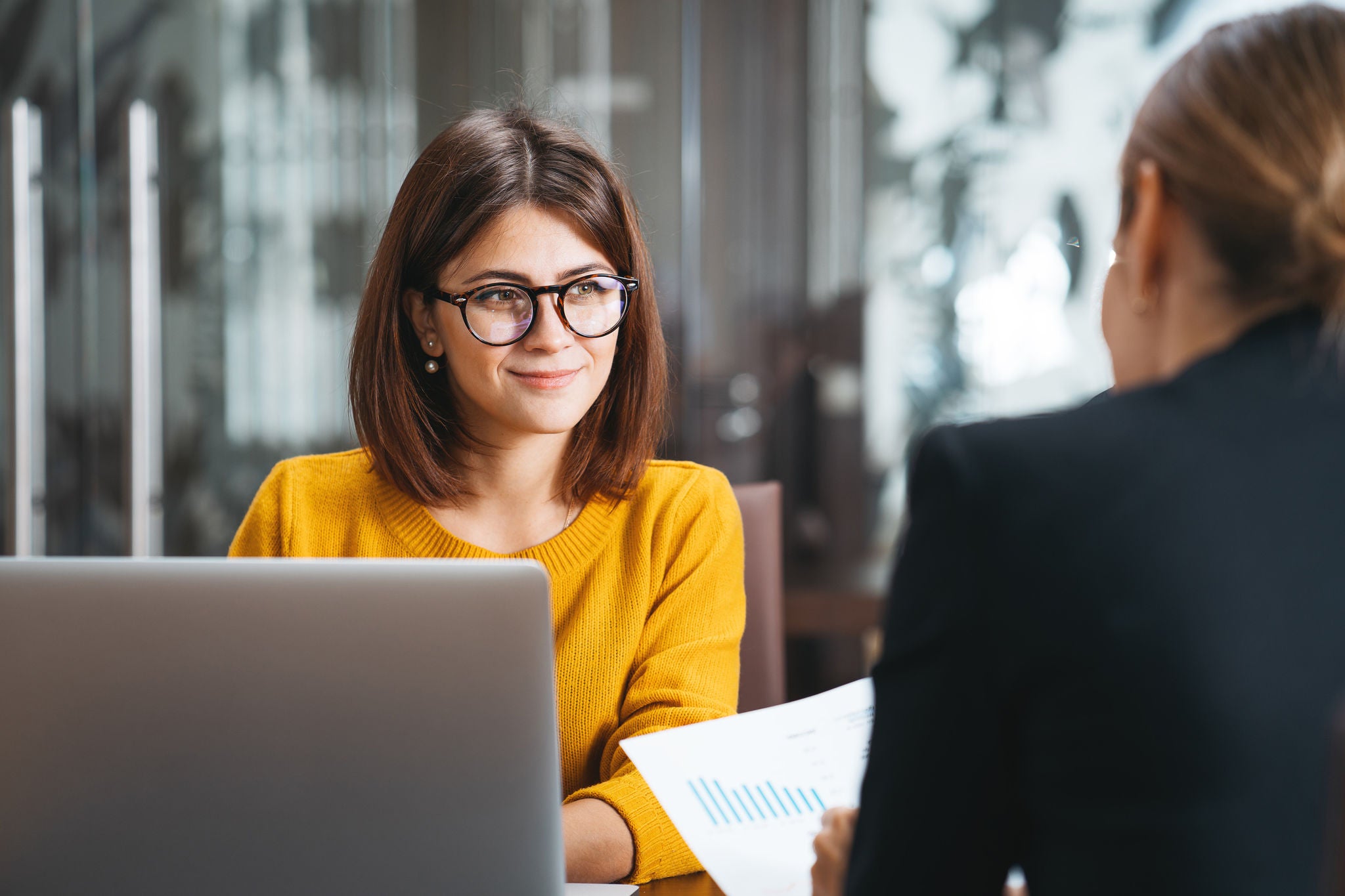 Dos mujeres trabajan juntas con una computadora portátil comparando documentación