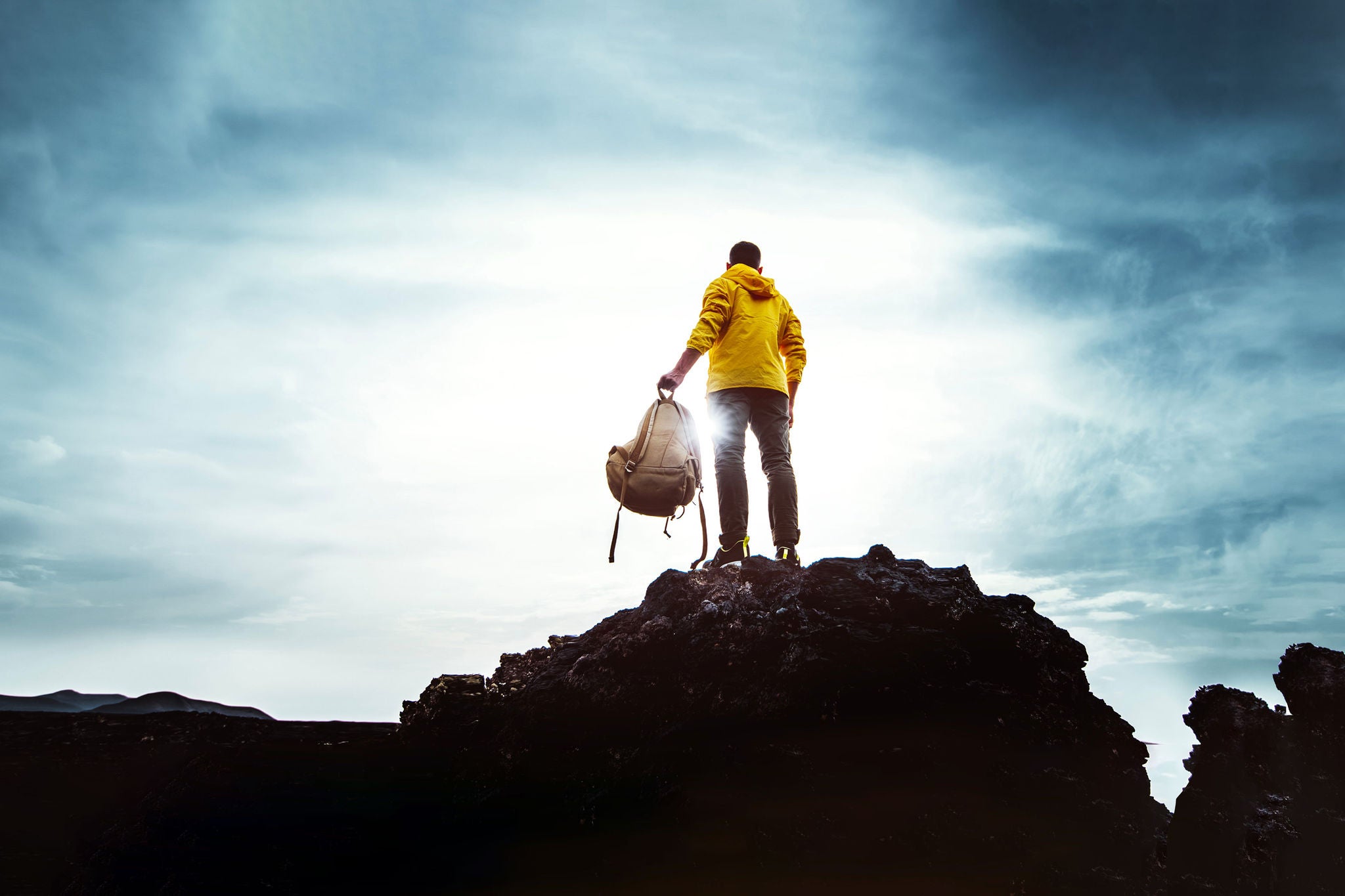 Young man with backpack standing on the top of a mountain at sunset  Goals and achievements