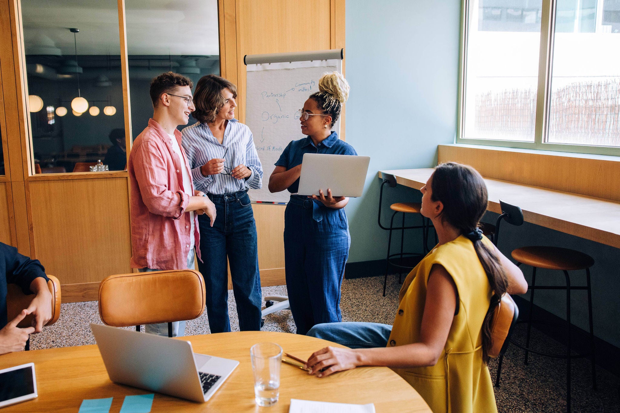 A diverse group of young professionals exchanging ideas in an office setting, including laptops and presentation materials. A collaborative approach to professional development and innovation.