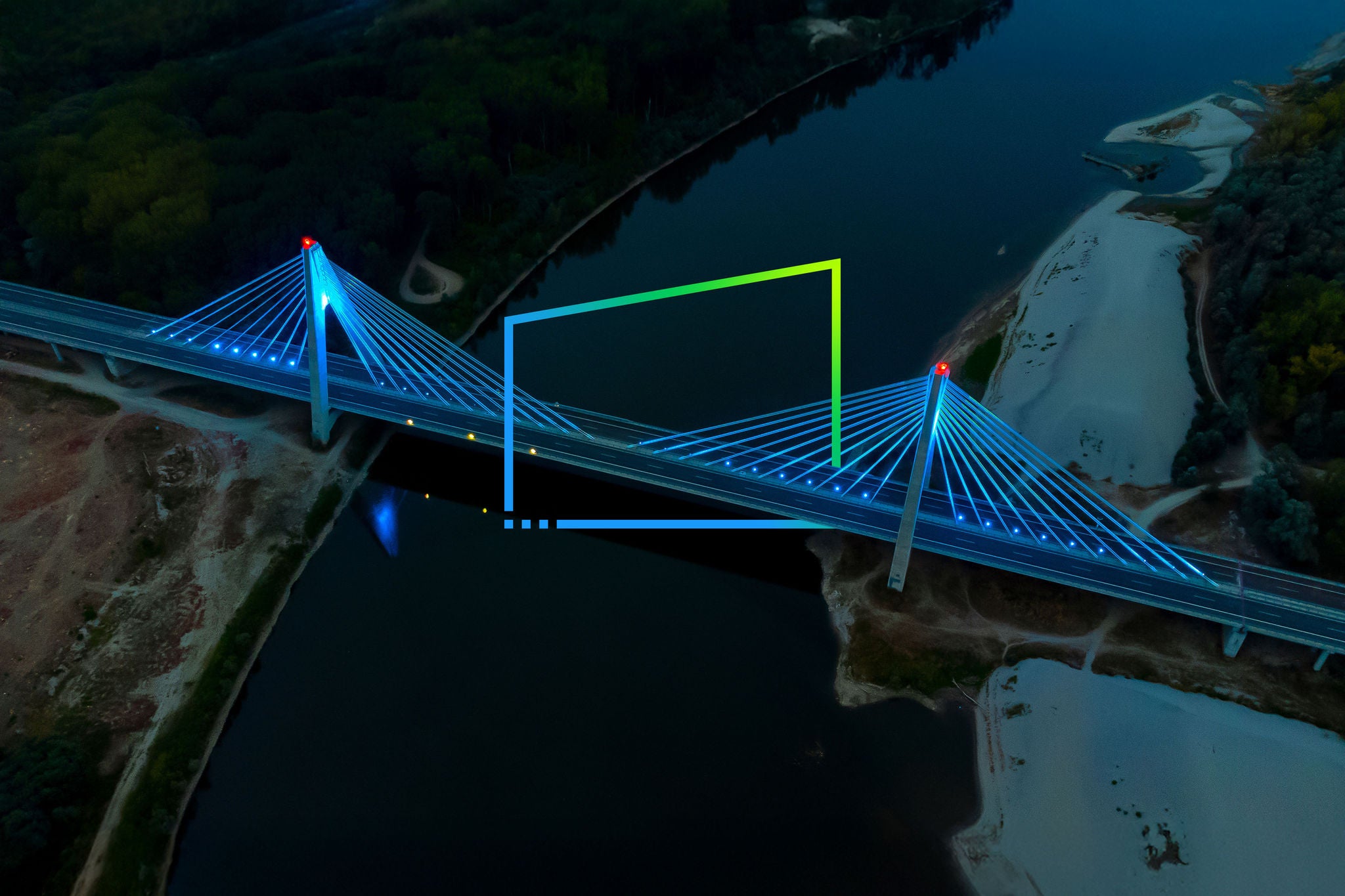 Aerial view of the illuminated cable-stayed bridge over the dark river