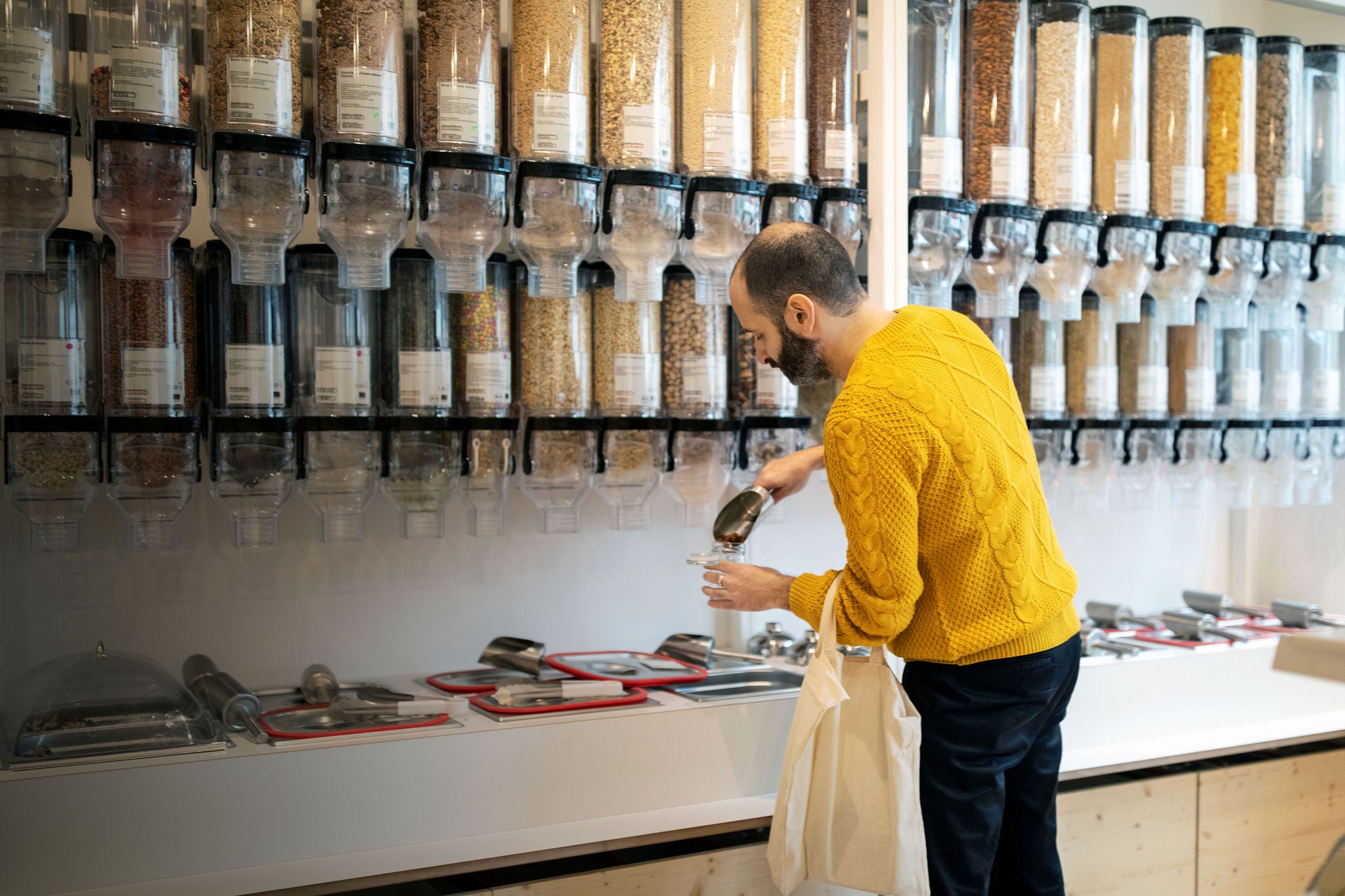 Man filling jar with serving scoop by containers at zero waste store