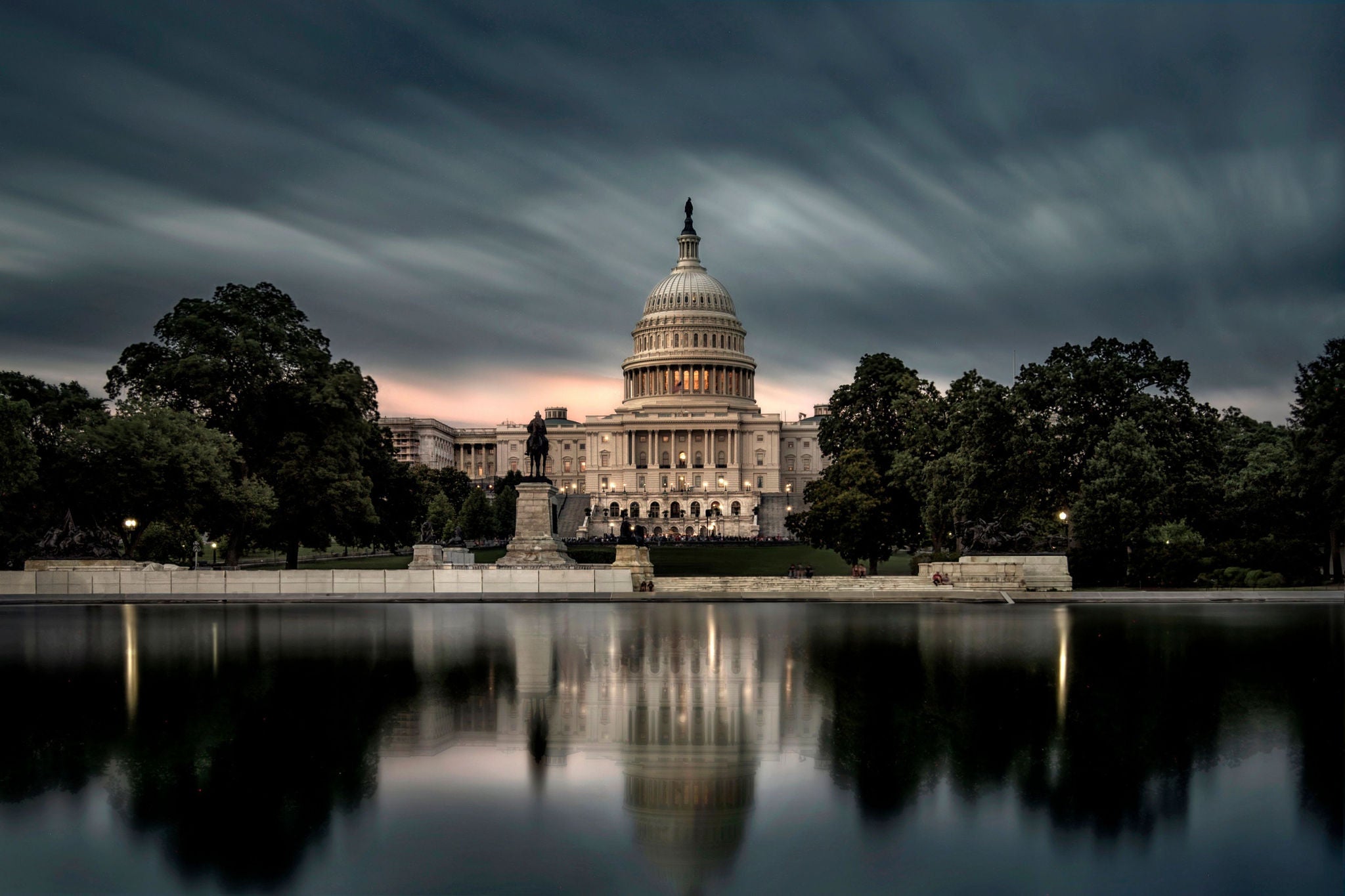 US Capitol building reflected in water beneath dramatic evening clouds.