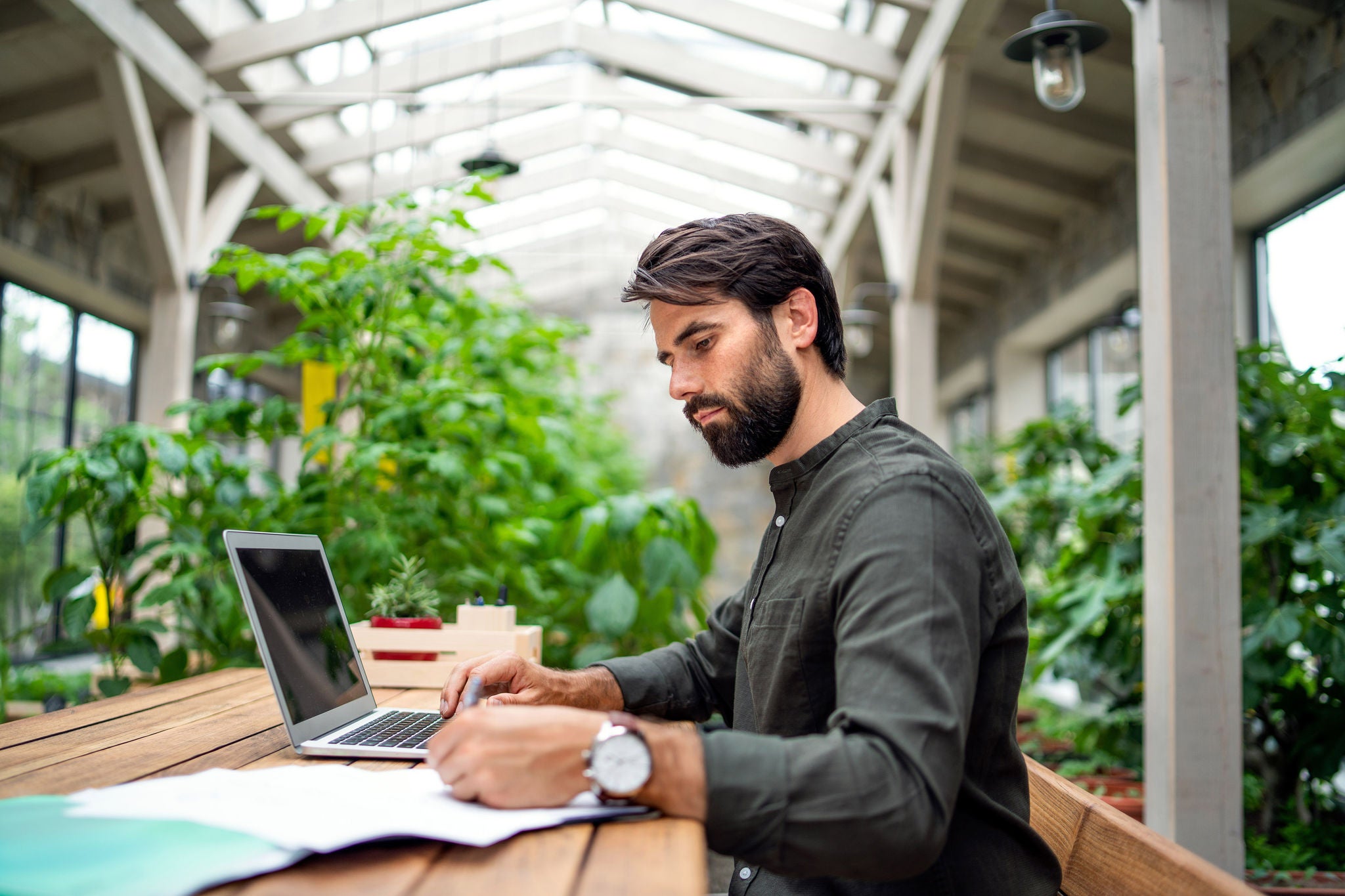 Young man works on a laptop at a wooden table in a green indoor office