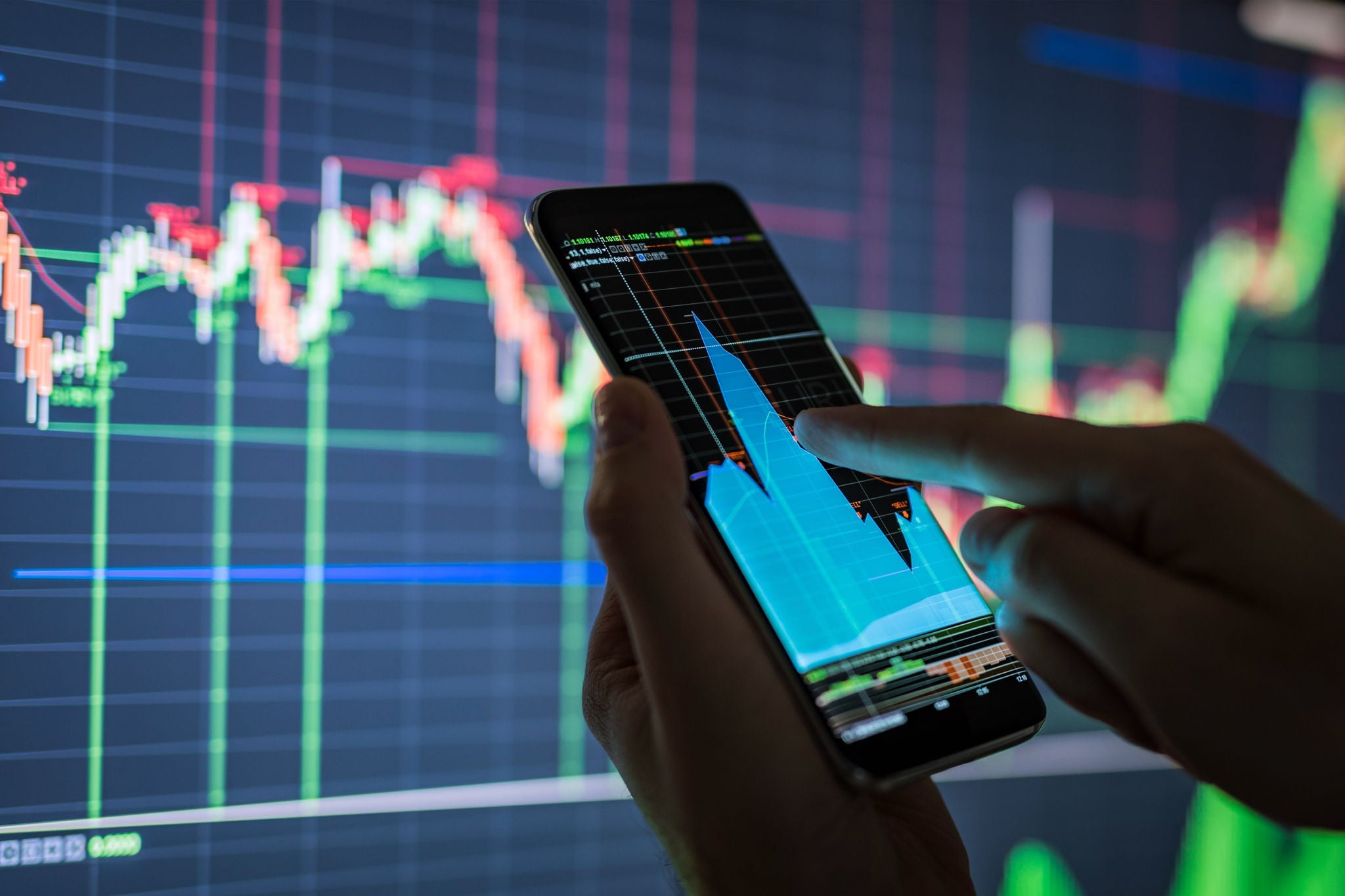 Hands interacting with chart on mobile phone in front of larger colorful line chart