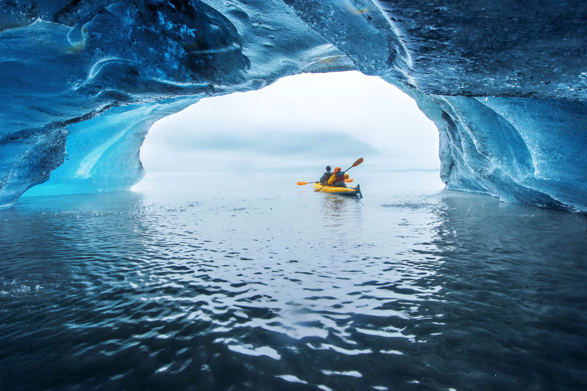 Two people kayaking out of an ice cave into open water