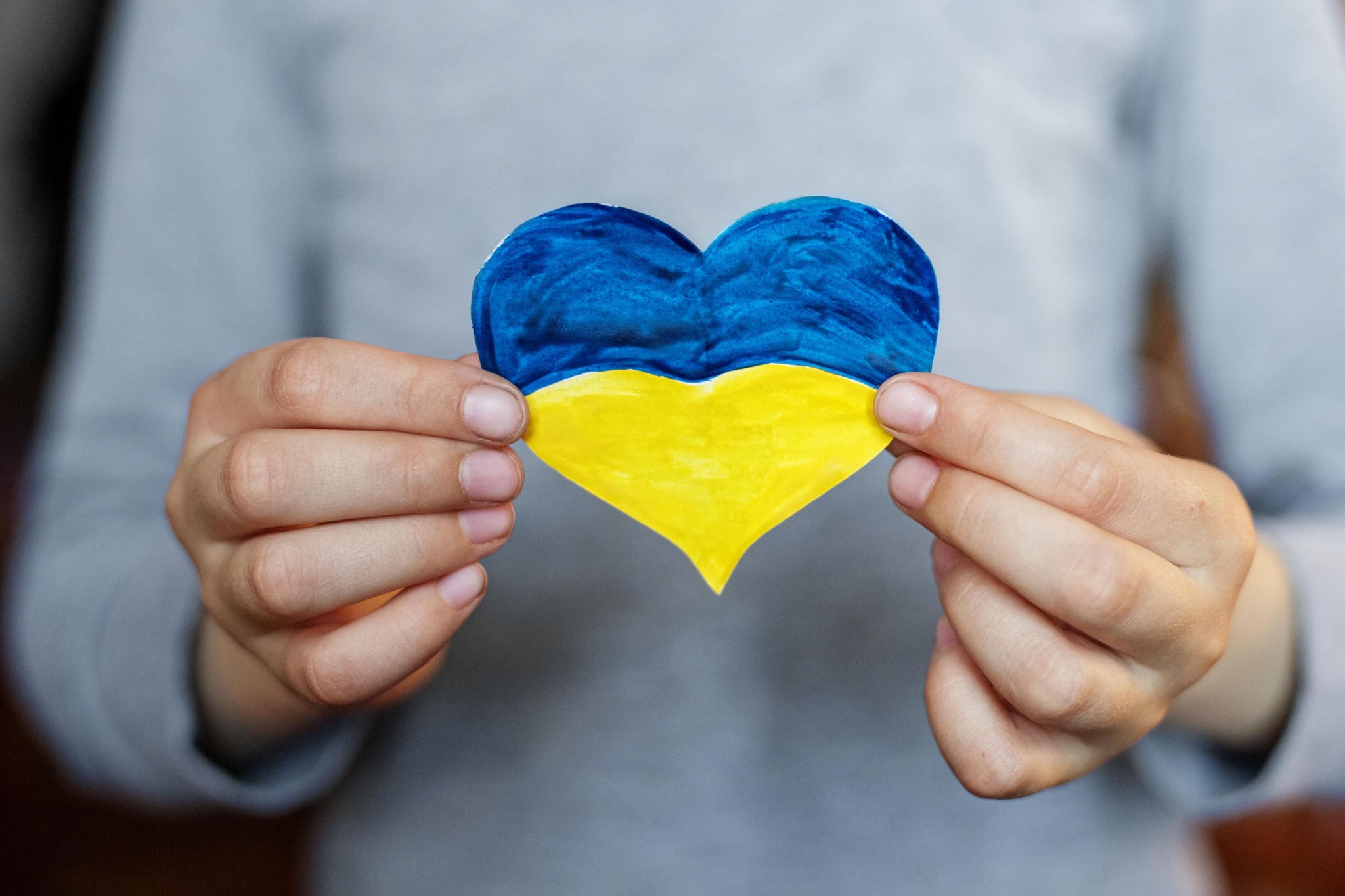 A smiling young woman with headphones and folders, standing outdoors on a college campus.