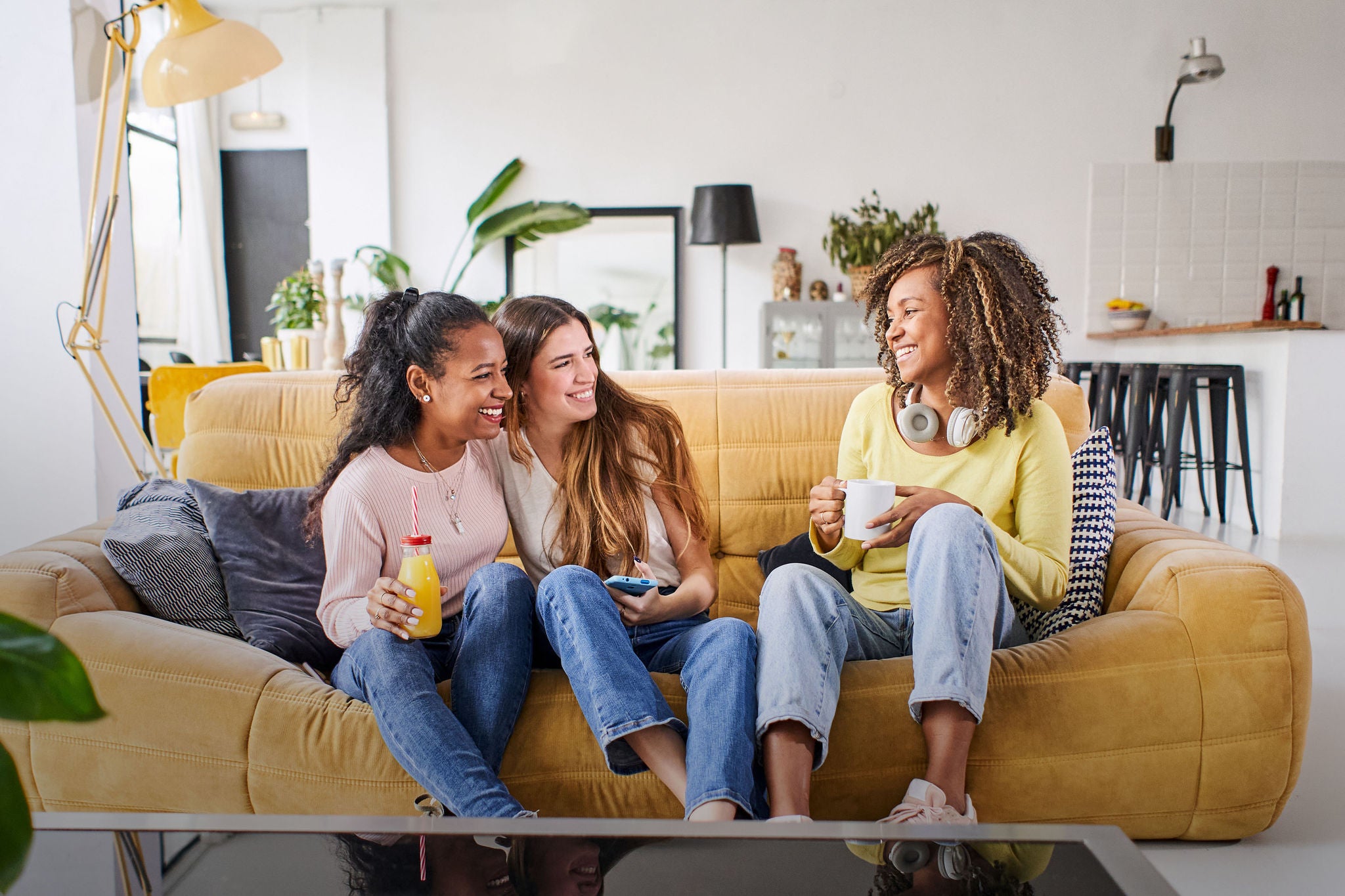 Three female friends smiling on a sofa at home, celebrating with juice and coffee, high-quality photo