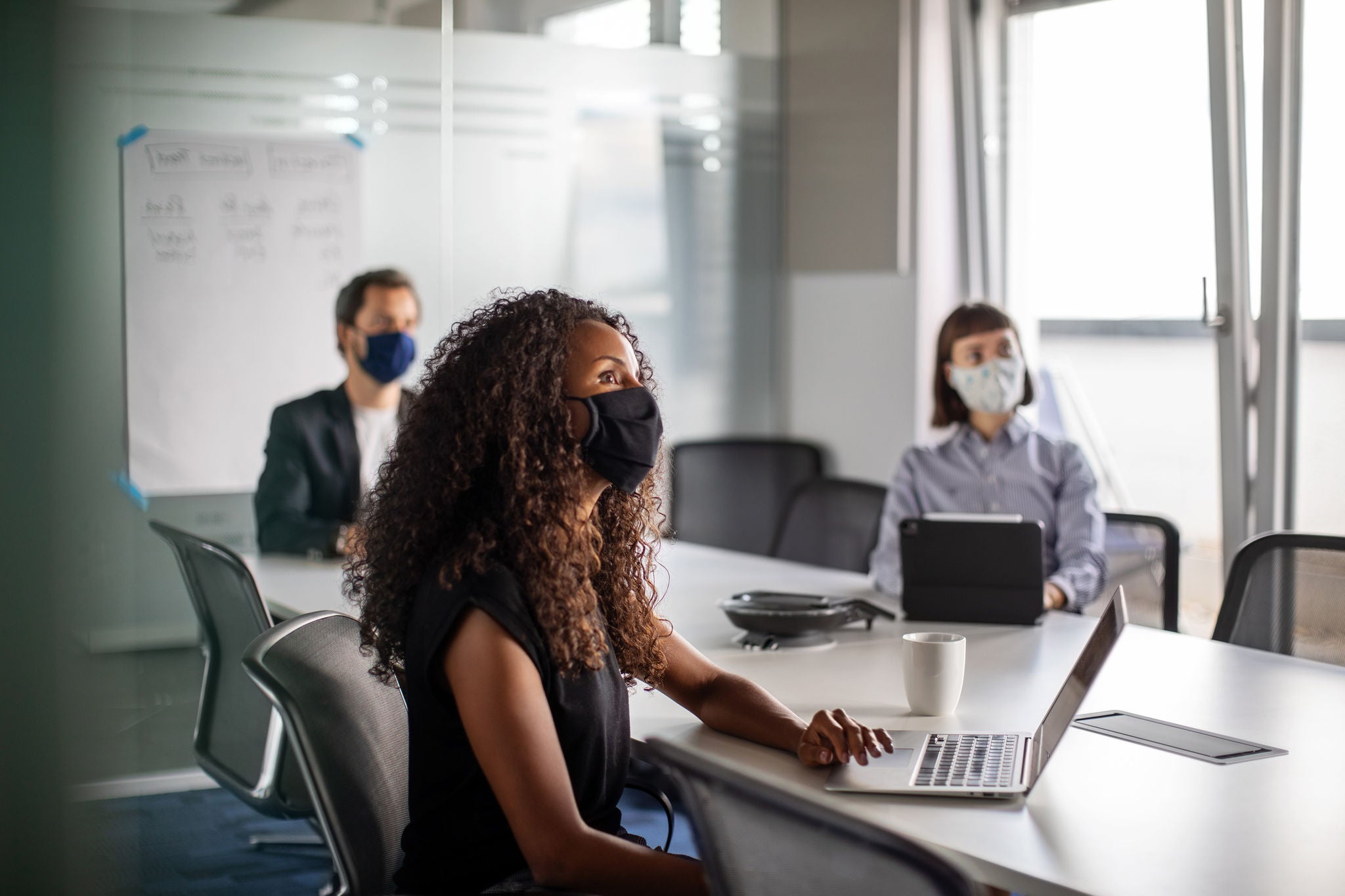Team of business professionals wearing face mask sitting in office boardroom during a meeting. Business people having meeting during pandemic.