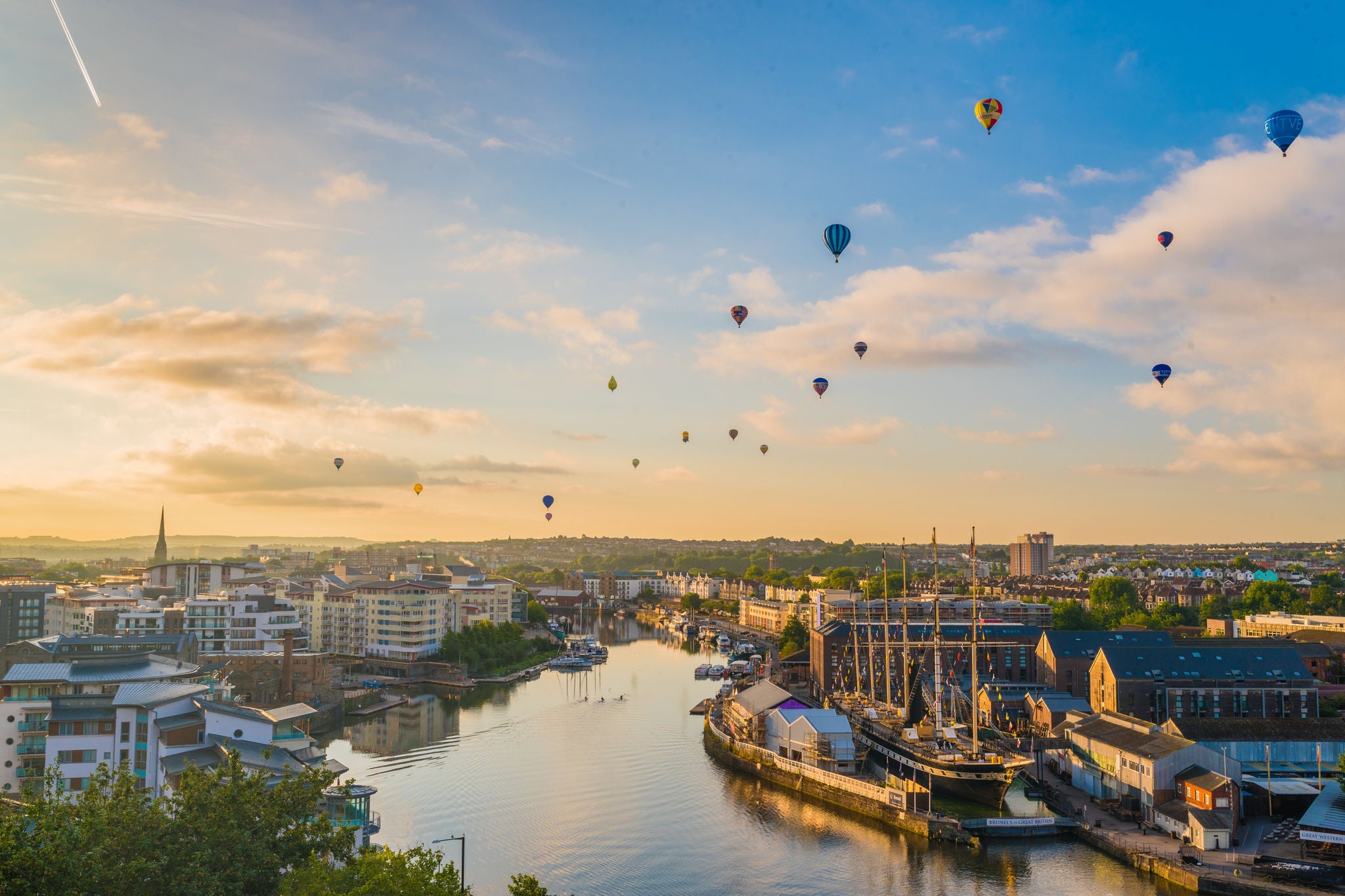 Hot air balloons floating above a river and city at sunset