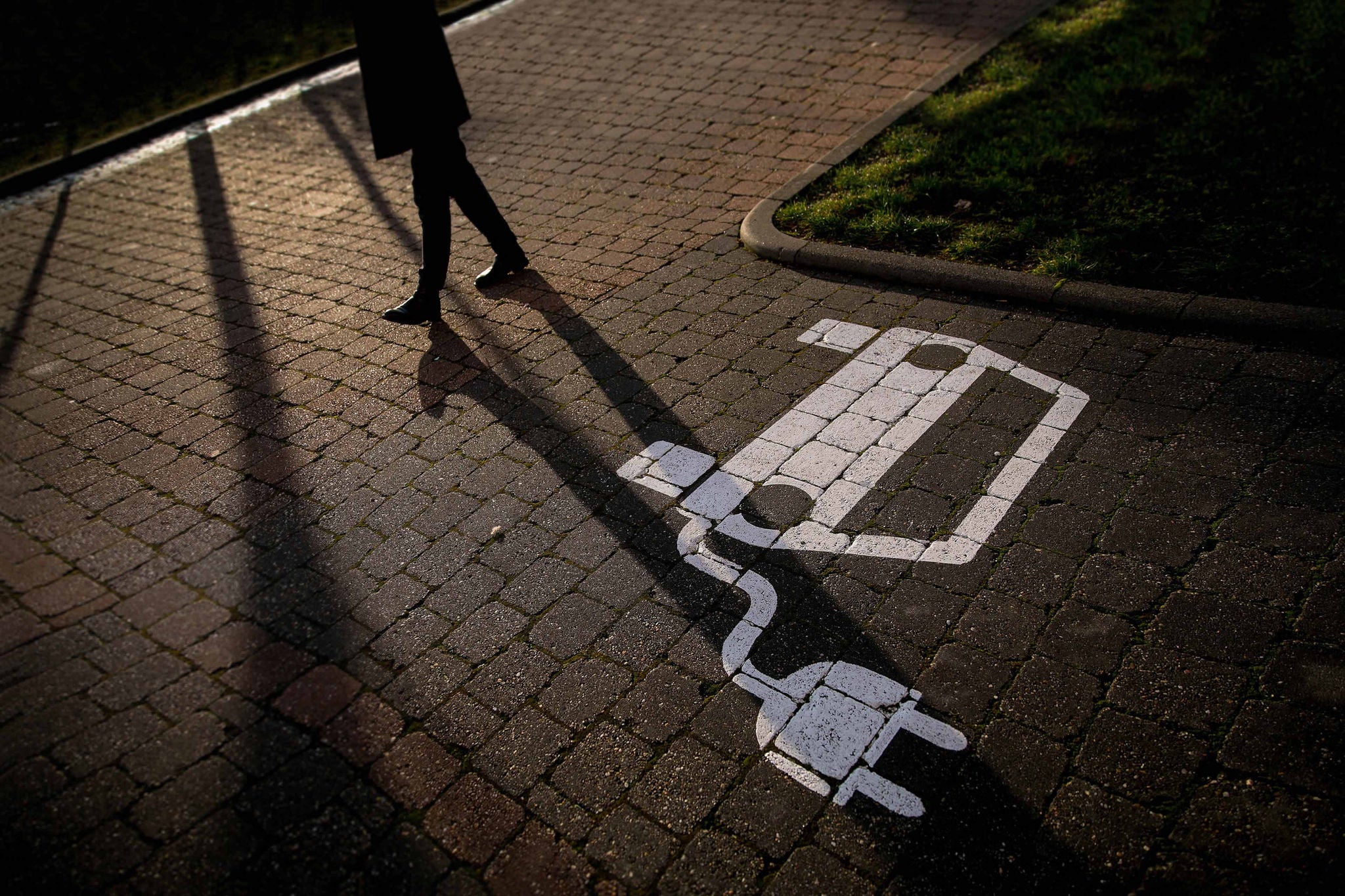 Schatten einer Person neben E-Auto-Ladesymbol am Boden