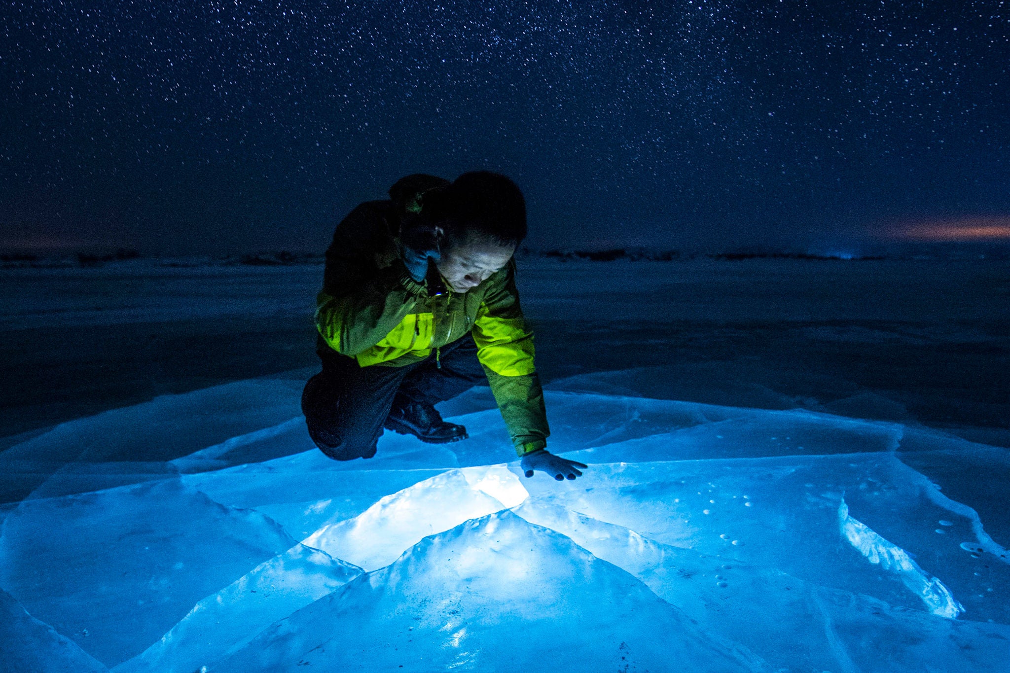 Mand lyser med lygte ned gennem isen på en fossen sø en stjerneklar vinteraften