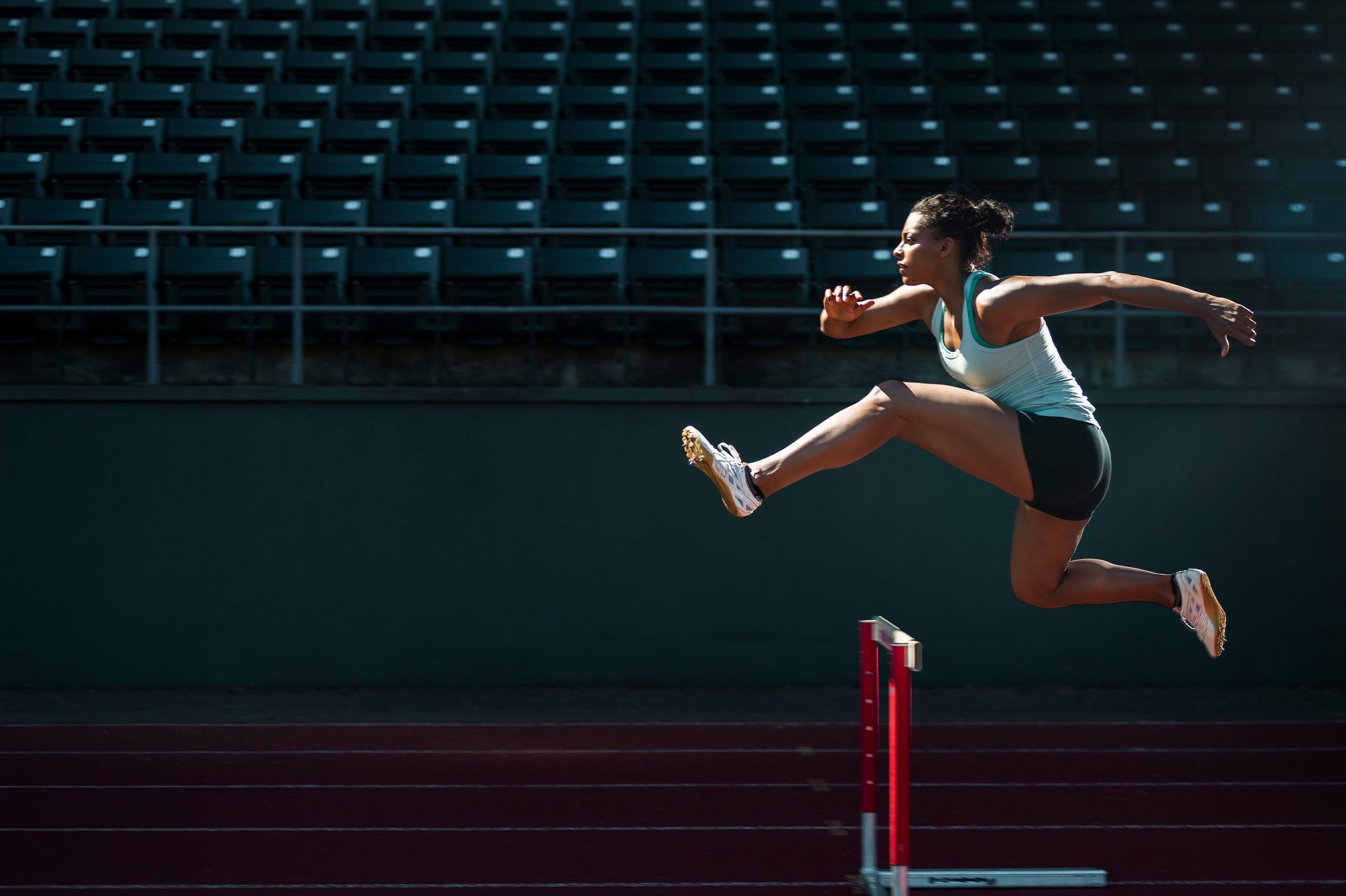 Eine Person überspringt eine Hürde auf einer roten Laufbahn, kraftvoller Sprung in einem leeren Stadion. weit und ruhig.