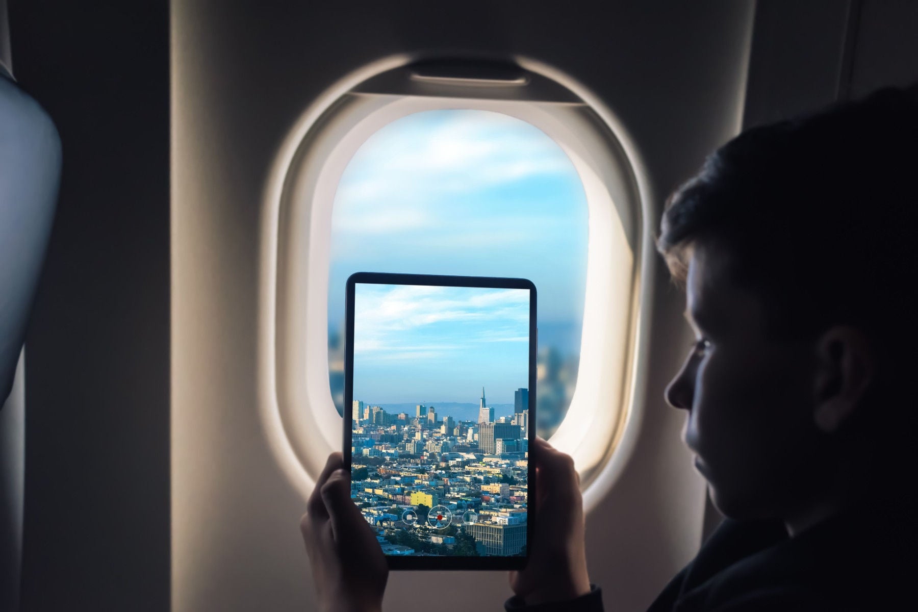 Ey caucasian boy using tablet pc taking picture through airplane window